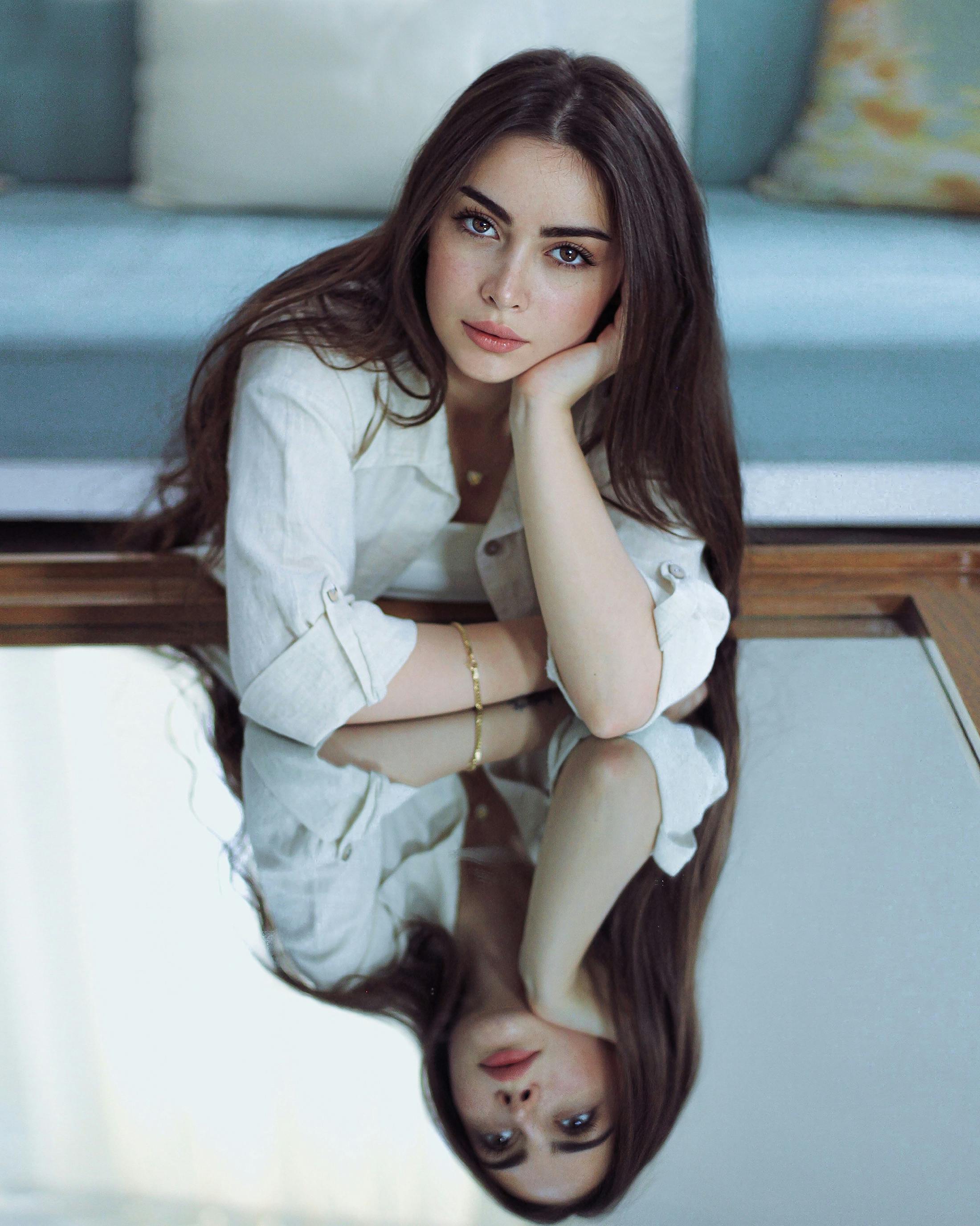 Stylish portrait of a woman with long brown hair reflected on a mirrored surface indoors.