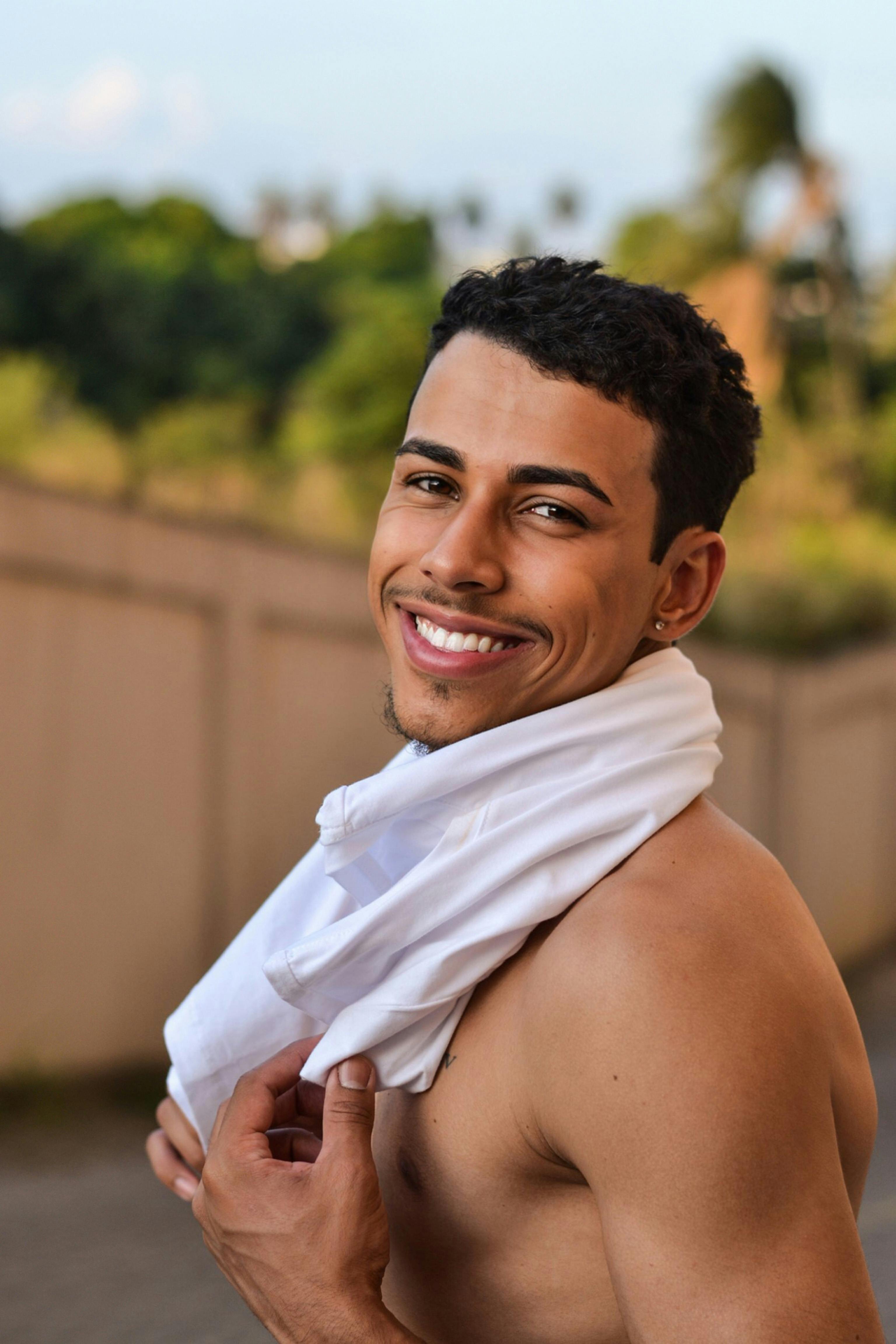 A cheerful young man smiling outside in Sete Lagoas with a towel draped around his neck.