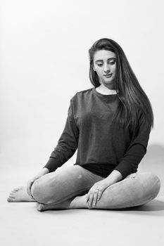 Elegant monochrome portrait of a young woman sitting cross-legged in casual attire.