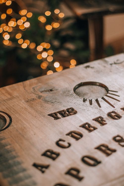 Free Close-up of a wooden Ouija board with decorative bokeh lights in the background. Stock Photo