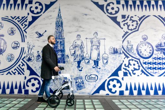 A man with a rollator passes a Delft-style mural in Delft, Netherlands.