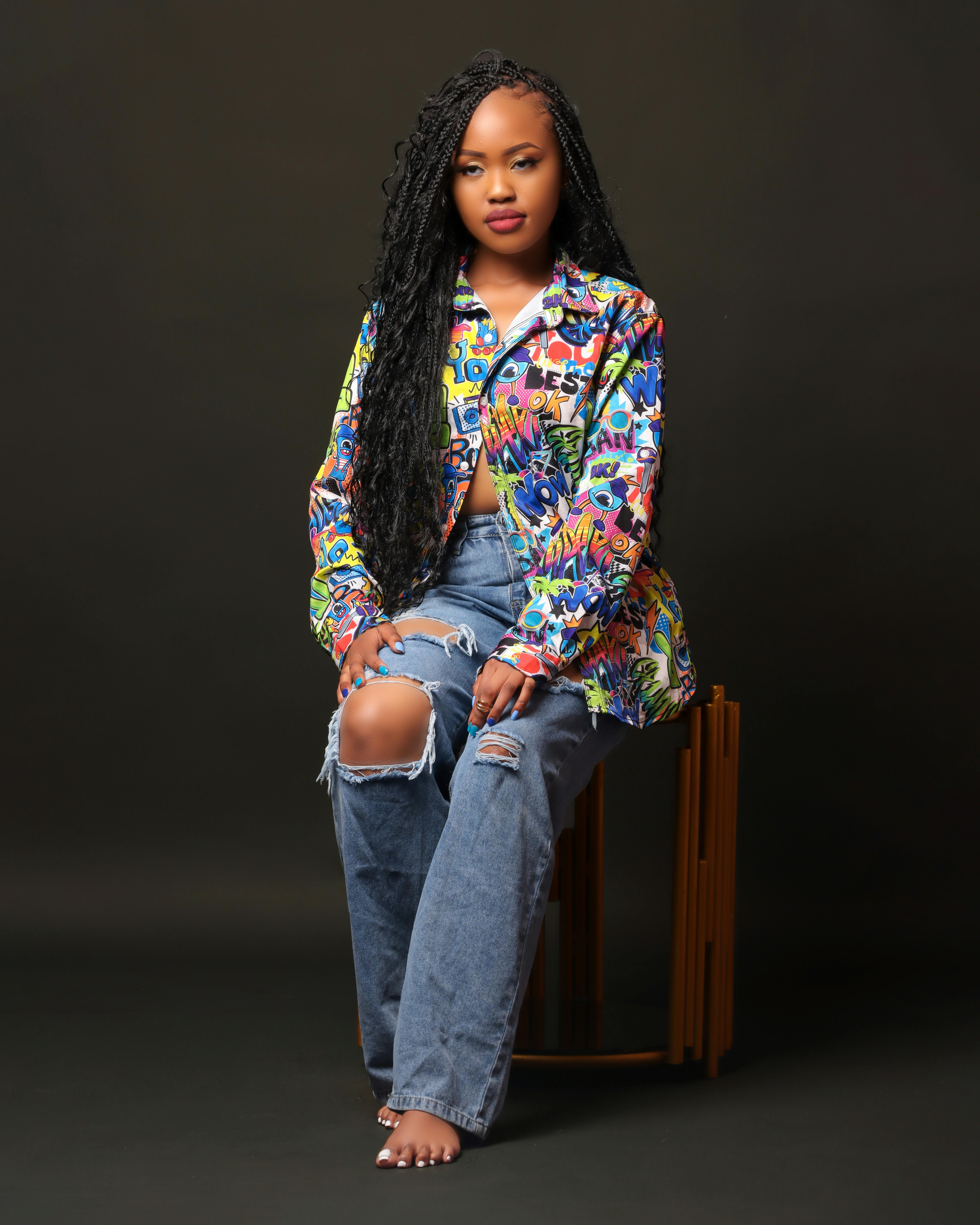 Free A young woman poses in a colorful jacket and ripped jeans against a dark background. Stock Photo