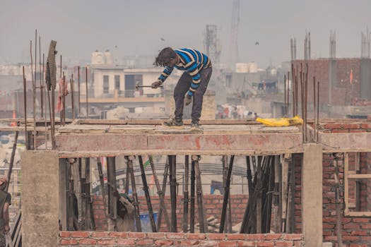 A construction worker standing on a building scaffold in an urban setting in New Delhi, India.