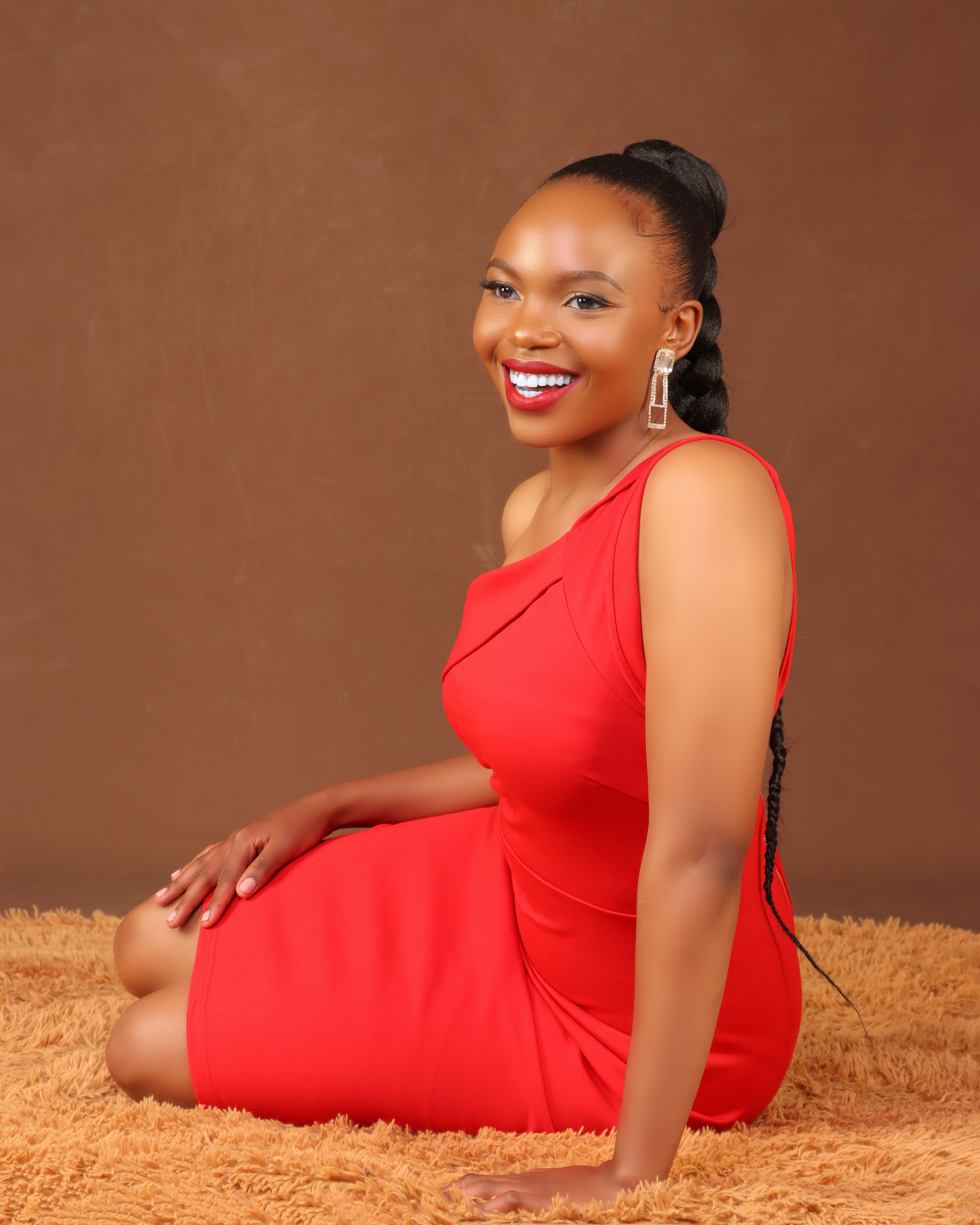 Stylish studio portrait of a smiling woman in a red one-shoulder dress, showcasing elegance.