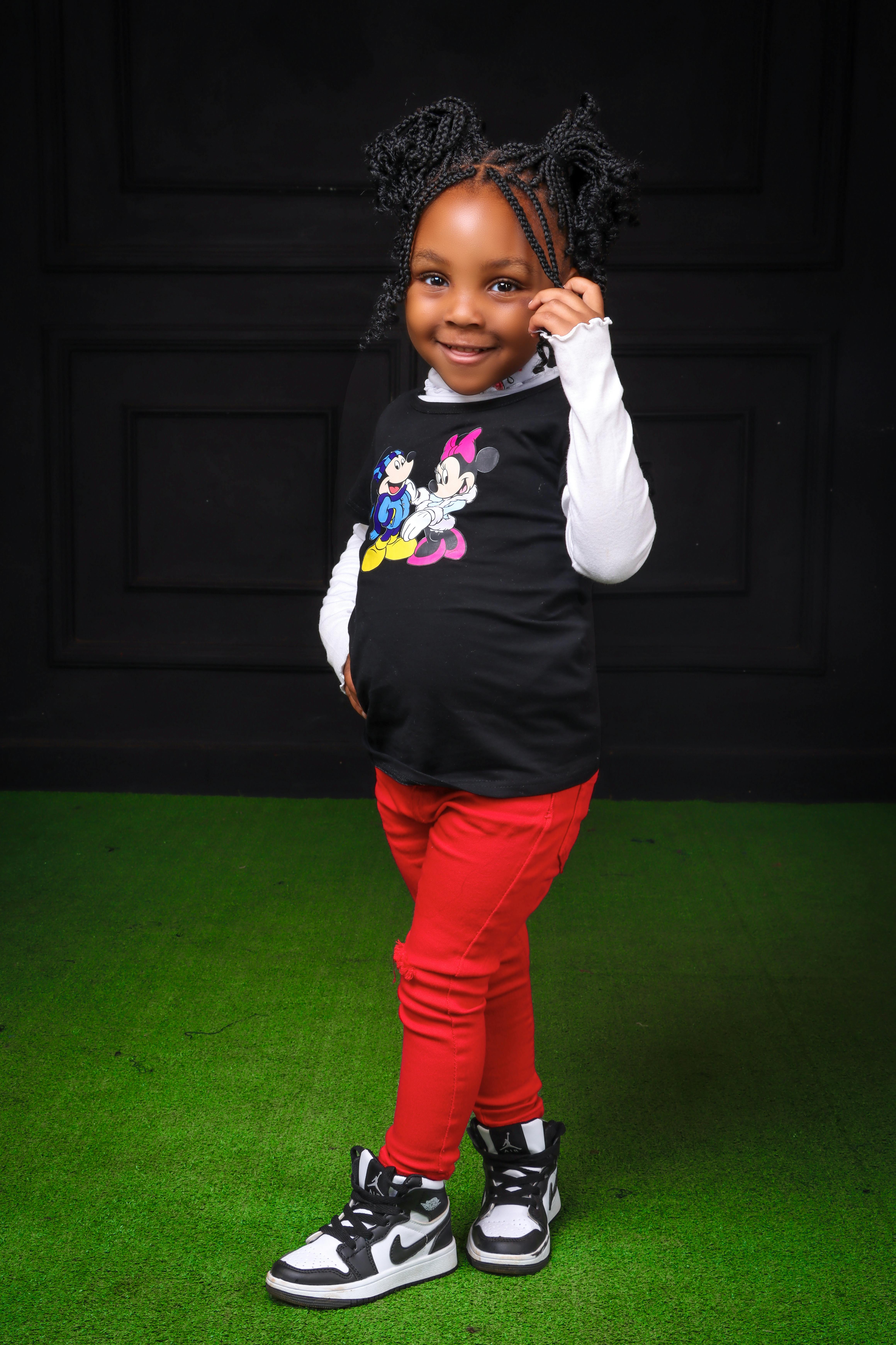 Adorable girl in fashionable attire posing with a smile in a studio setting.