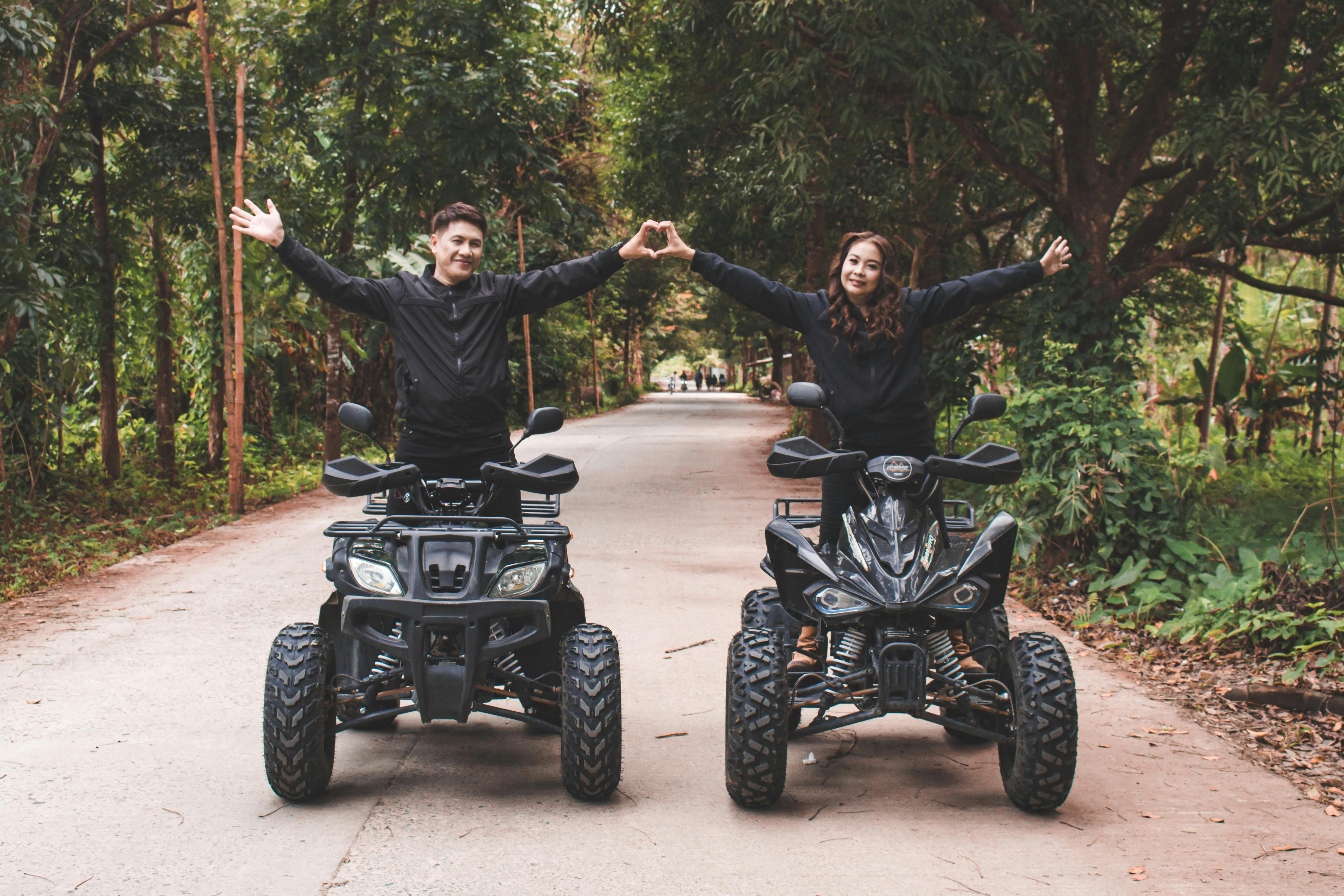 couple making hand heart while standing on quad bikes