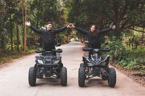 Couple Making Hand Heart While Standing on Quad Bikes