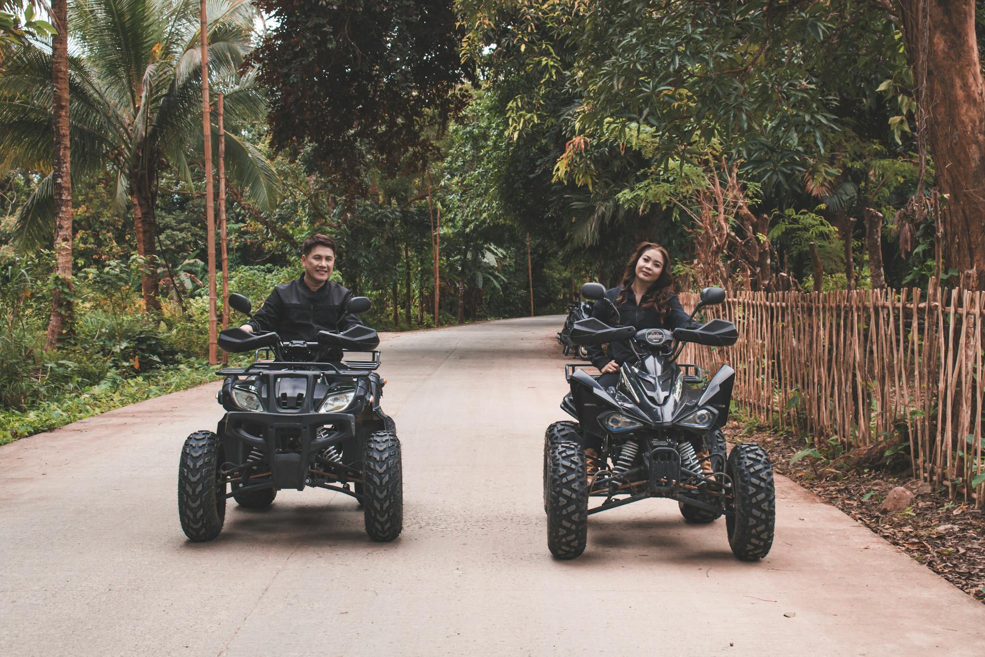 Asian couple riding quad bikes on a scenic outdoor road surrounded by lush greenery.