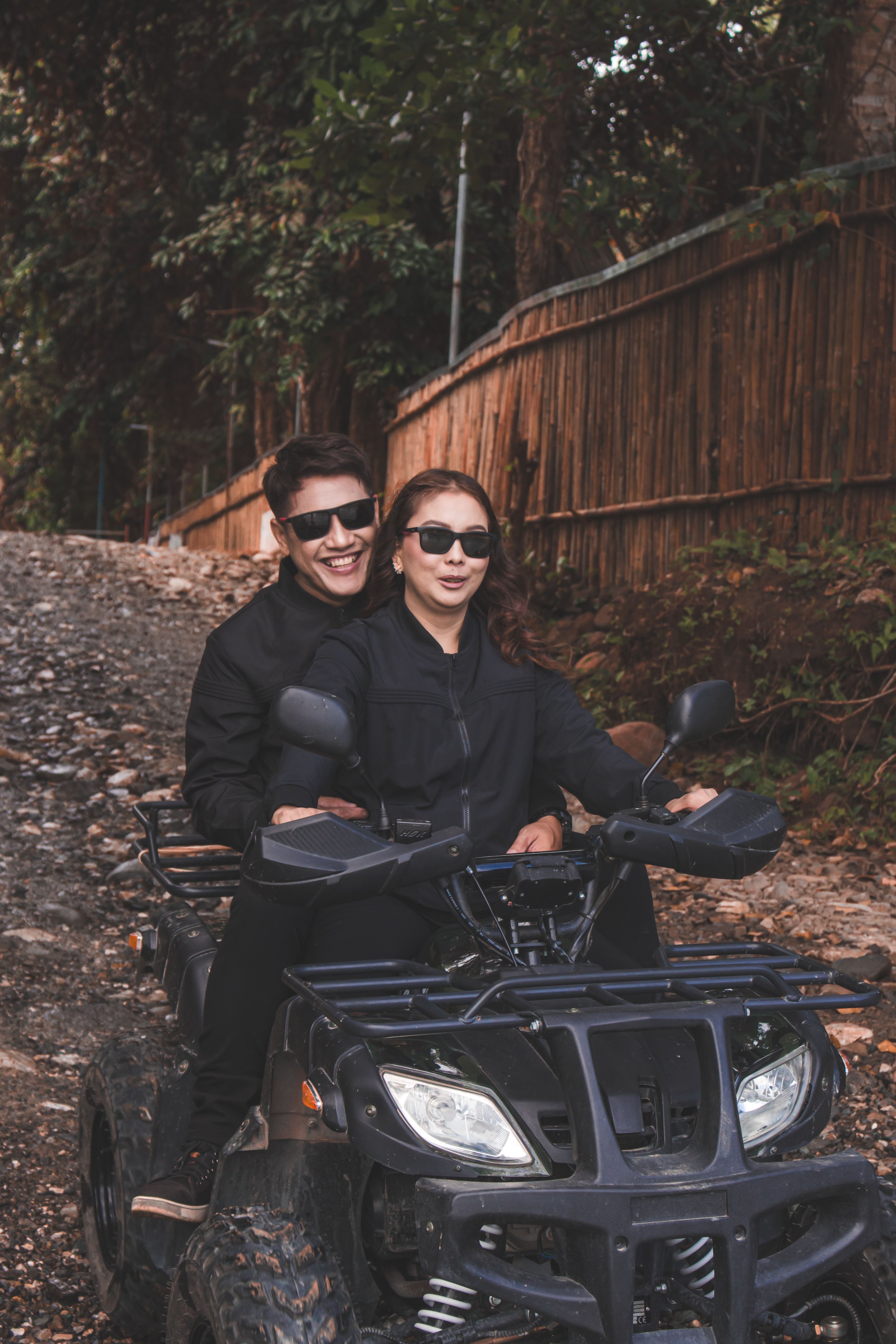 Smiling couple riding an ATV on a rural trail, enjoying outdoor adventure.