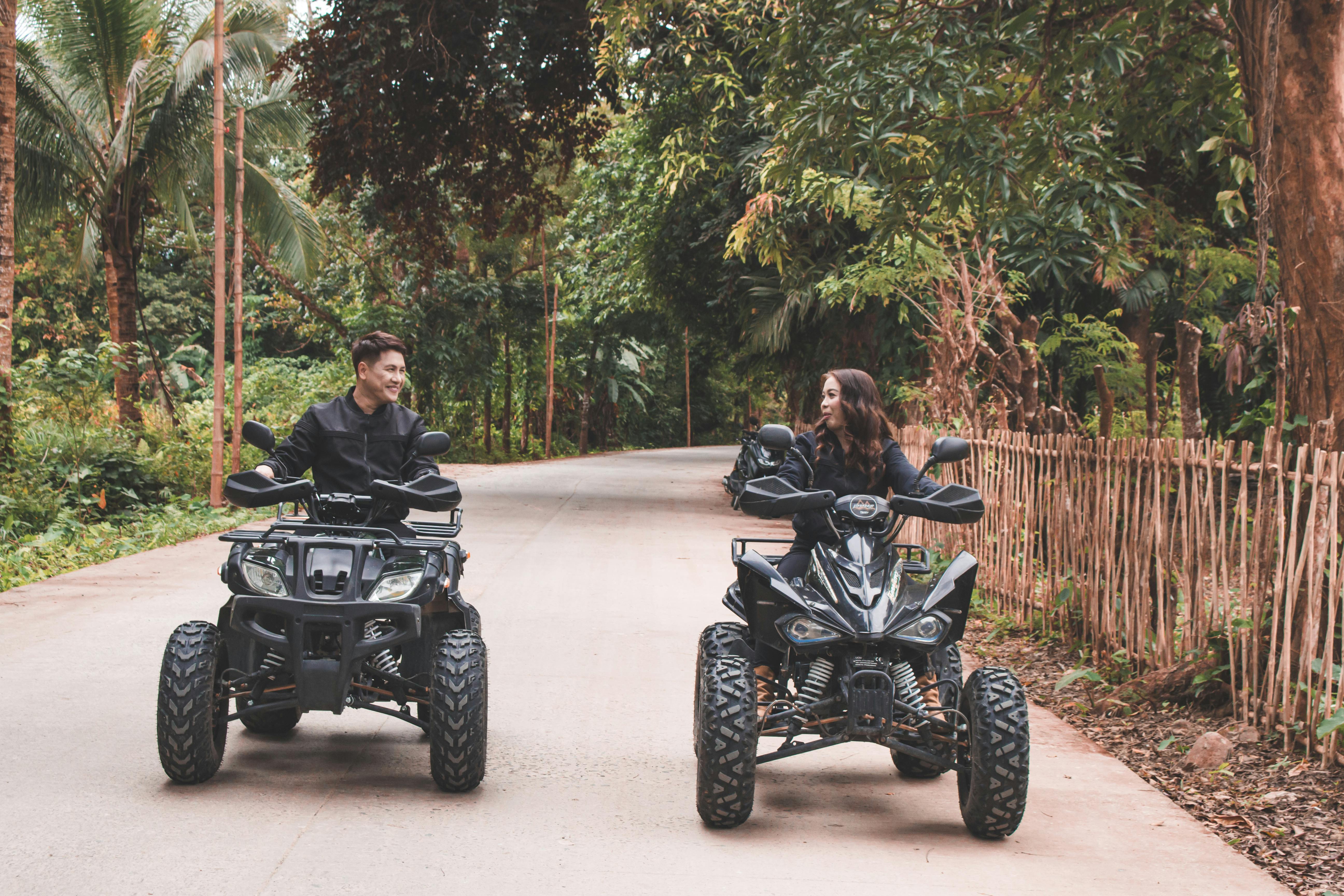 couple riding quad bikes on a road among palm trees