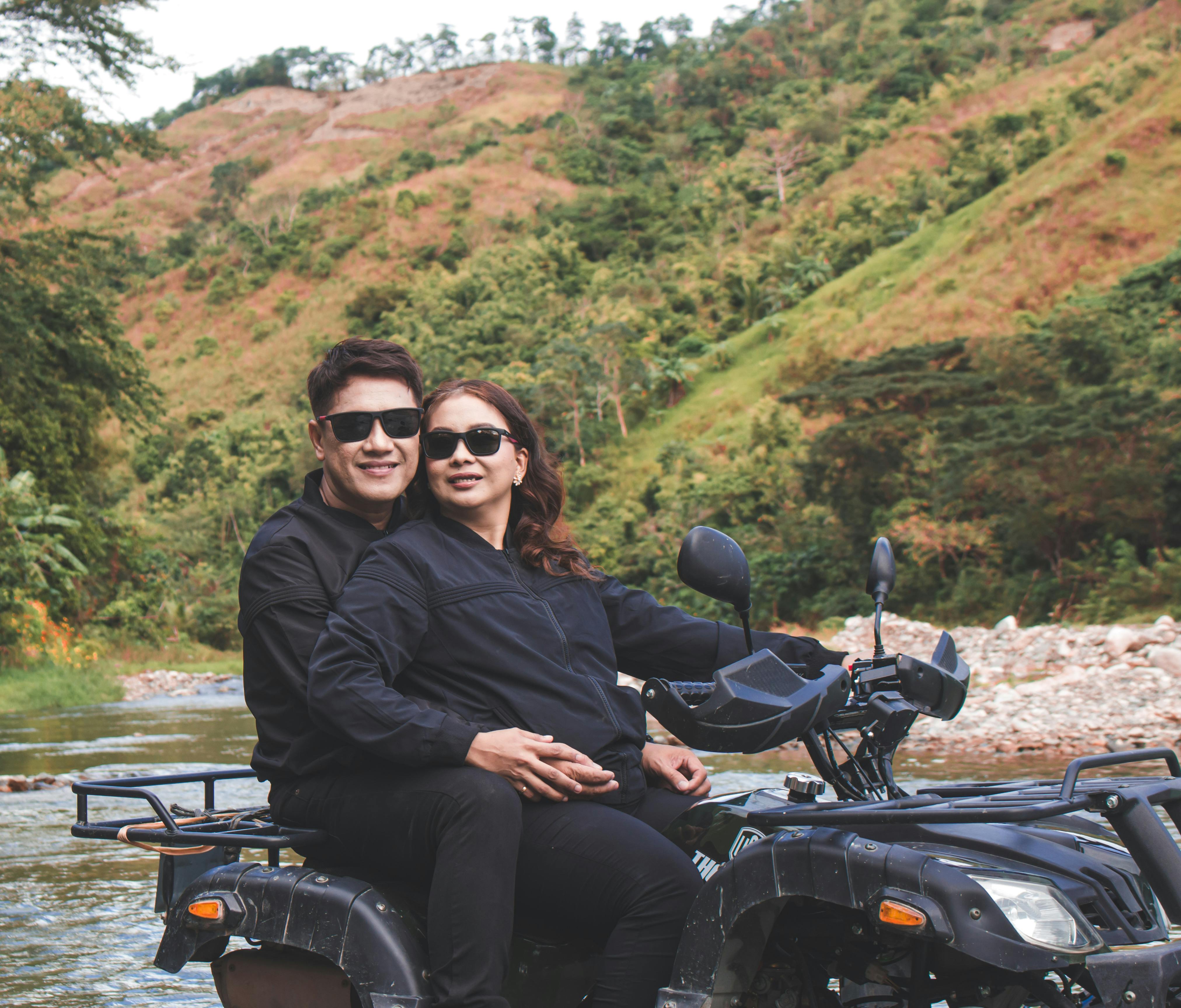 Couple embraces on quad bike by a river, enjoying a rural adventure.