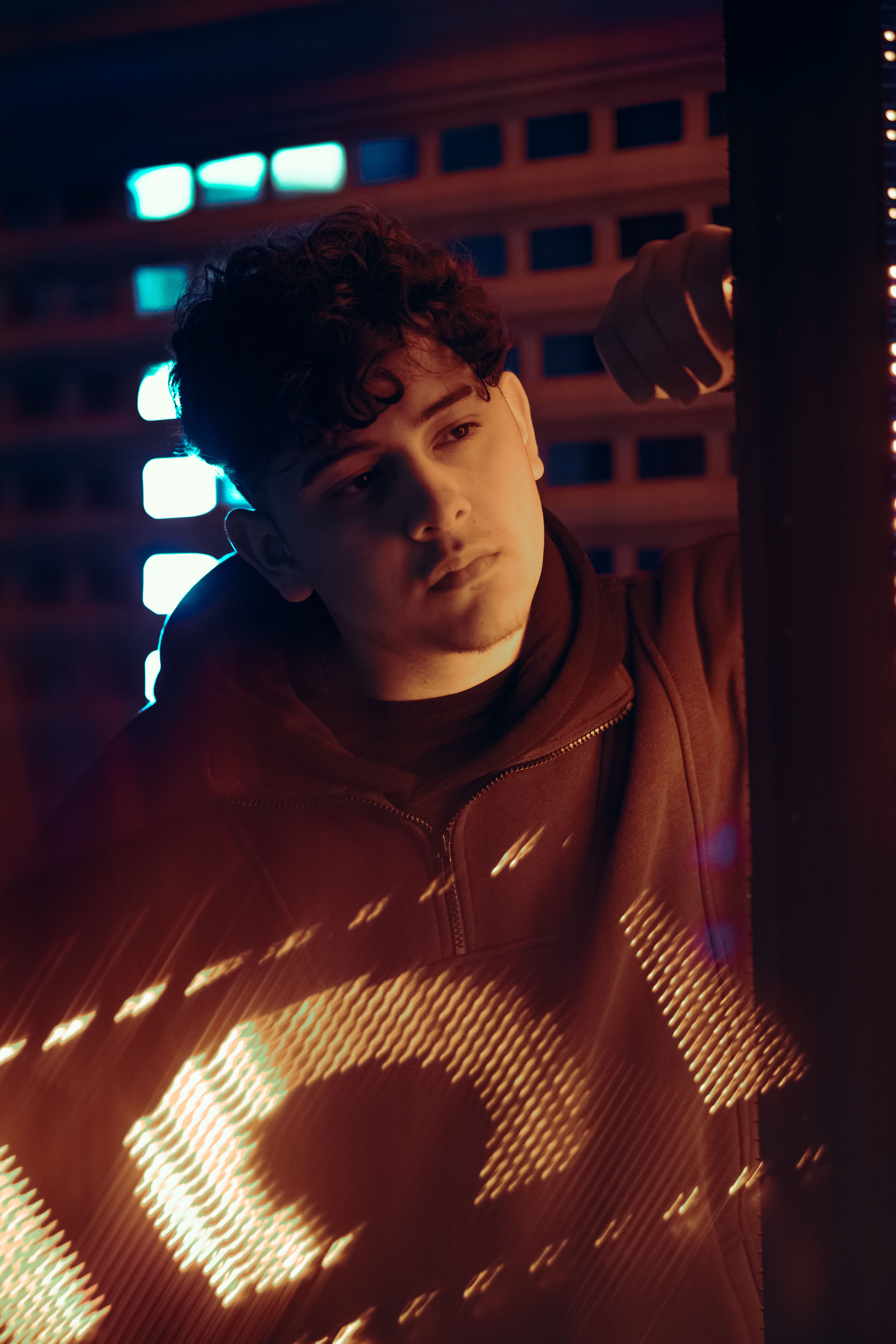 Portrait of a young man with curly hair standing in vibrant urban neon lights.