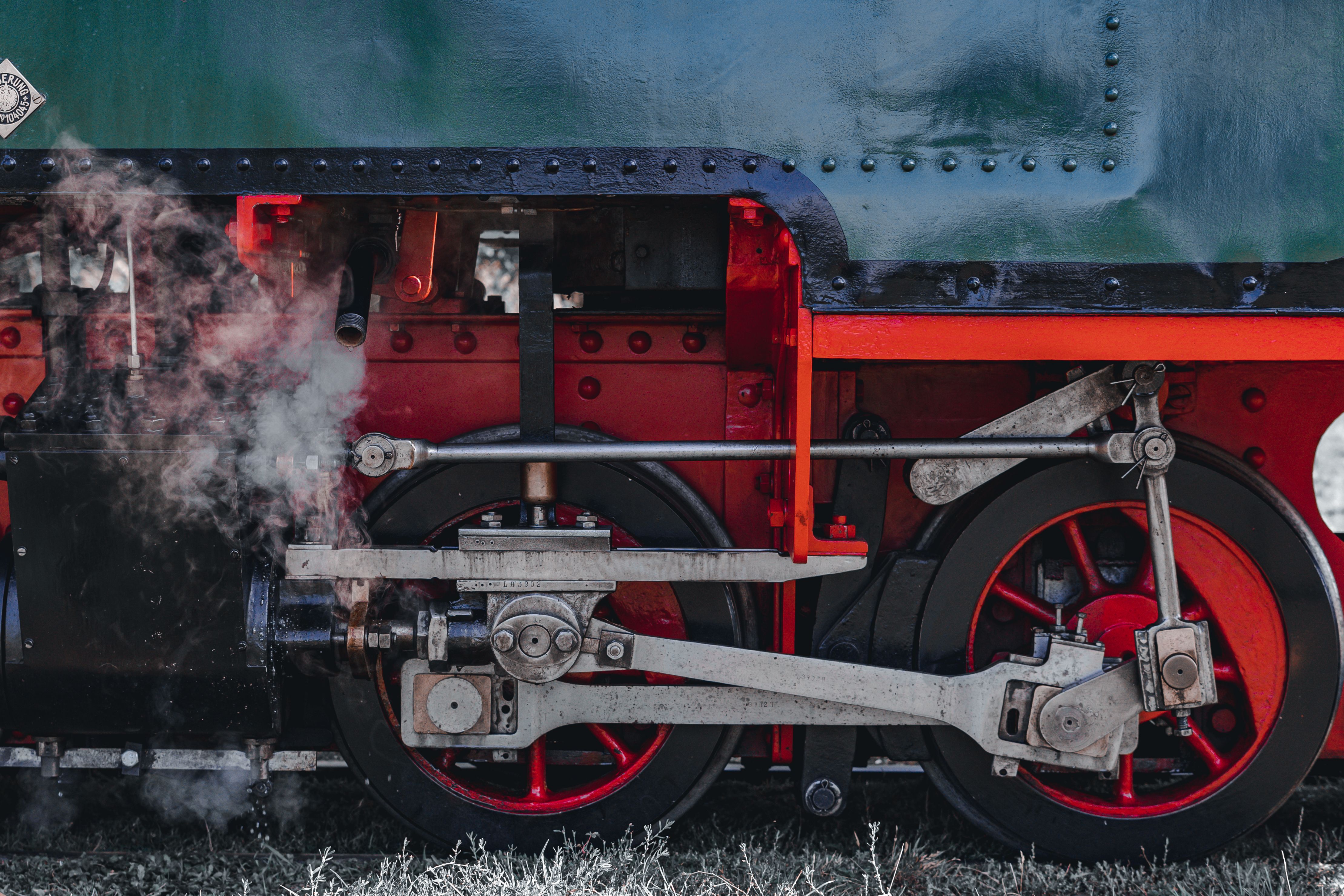 Detailed view of a steam locomotive's machinery and wheel emitting smoke.