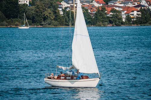 People Sailing on Sailboat on Lake in Town