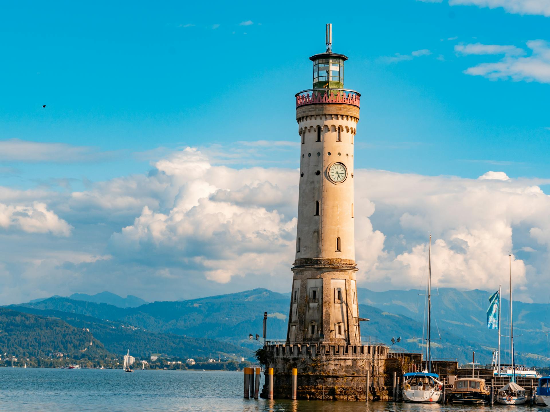 Charming lighthouse by the bay, with boats and mountains in the background under a clear blue sky.