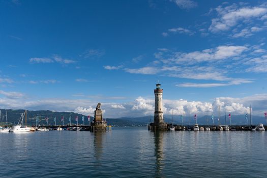 Beautiful view of Lindau Harbor with iconic lighthouse and statue, surrounded by calm lake waters.