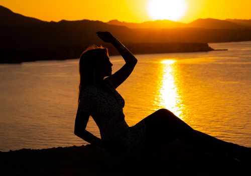 Free Silhouette of a woman by a lakeshore at sunset, highlighting tranquil scenery. Stock Photo