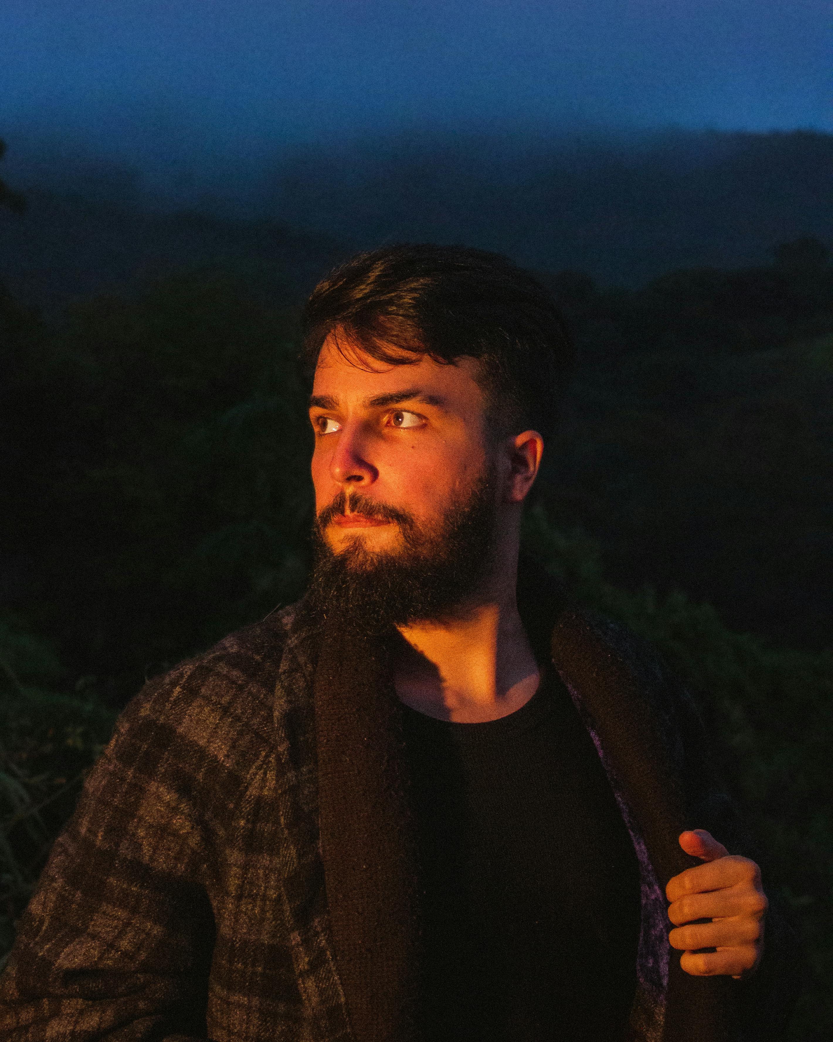 Bearded man in a checkered coat, highlighted against a night backdrop with moody lighting.