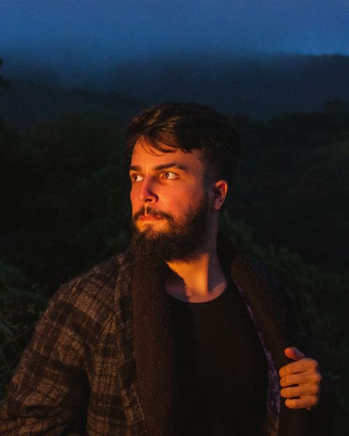 Free Bearded man in a checkered coat, highlighted against a night backdrop with moody lighting. Stock Photo