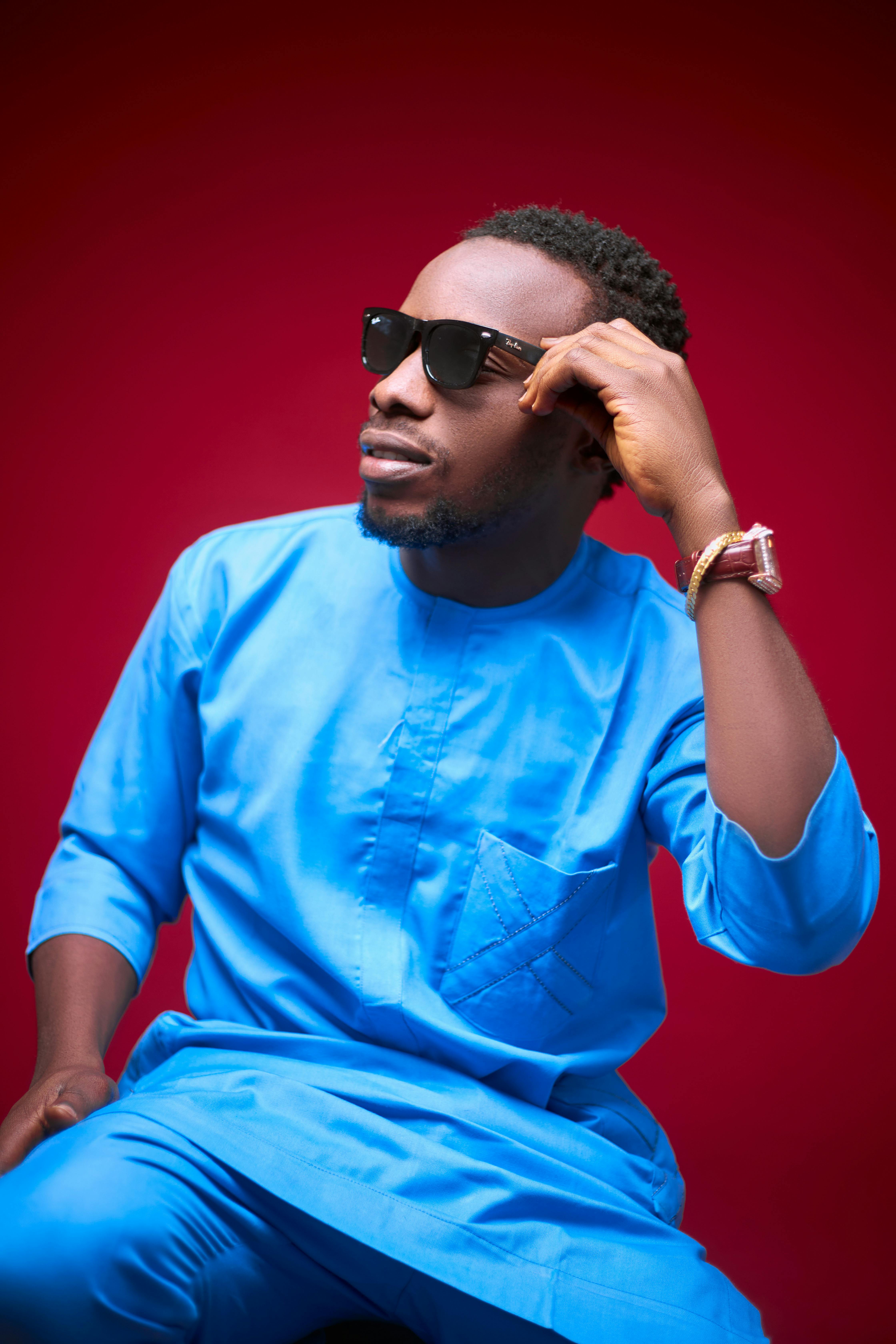 Fashionable man posing in blue attire against a red background, exuding confidence.