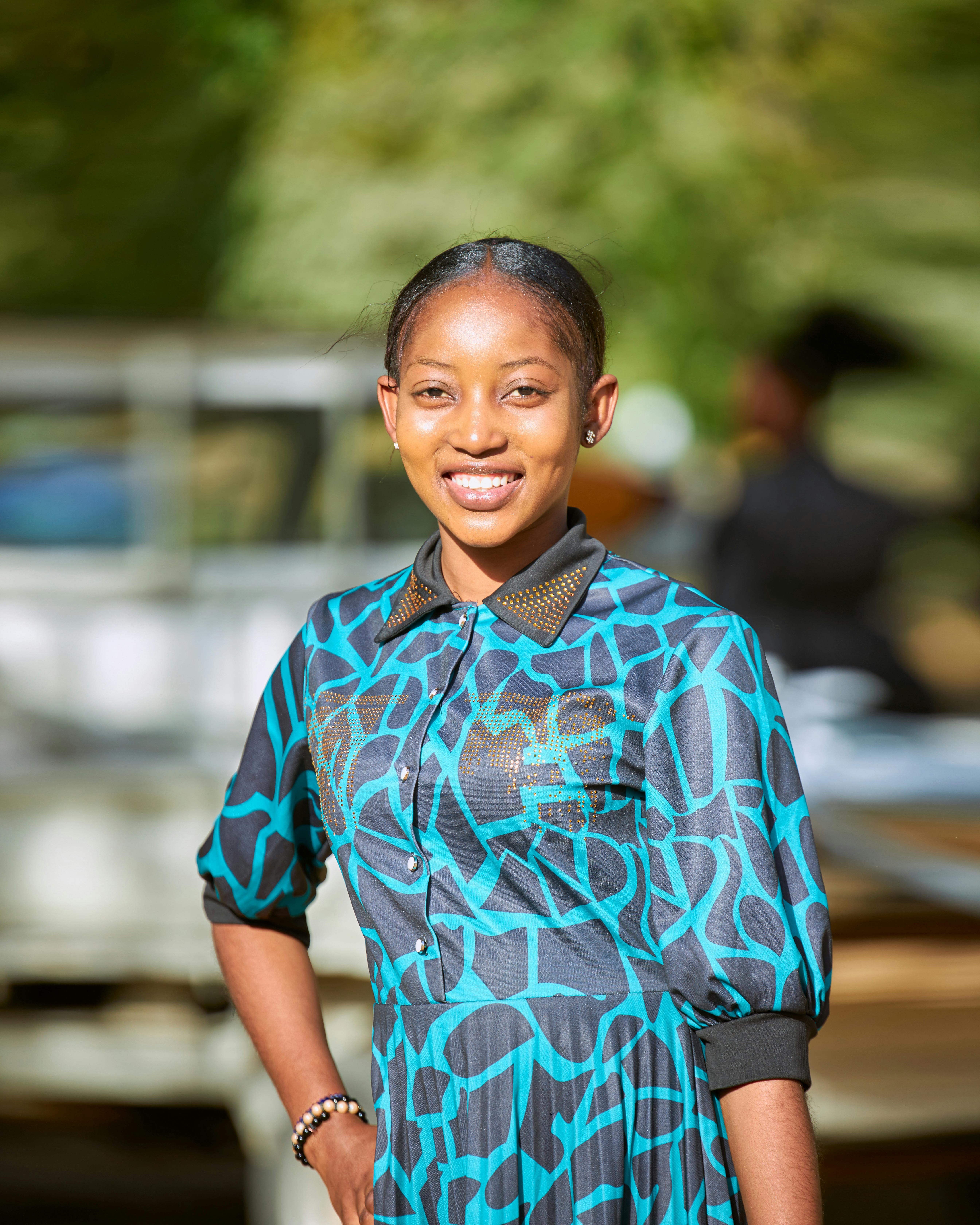 Portrait of a smiling woman in a stylish patterned dress outdoors, exuding confidence and joy.