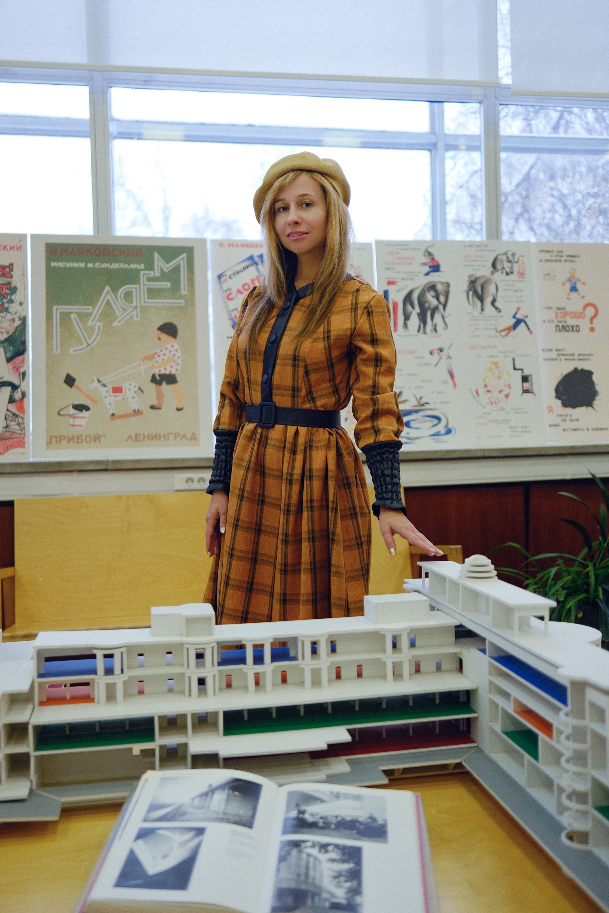 Stylish woman in a beret posing amidst educational materials and model buildings indoors.