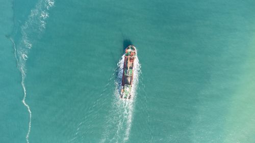 Free Drone shot of a cargo ship navigating through the calm turquoise waters near Somo, Spain. Stock Photo