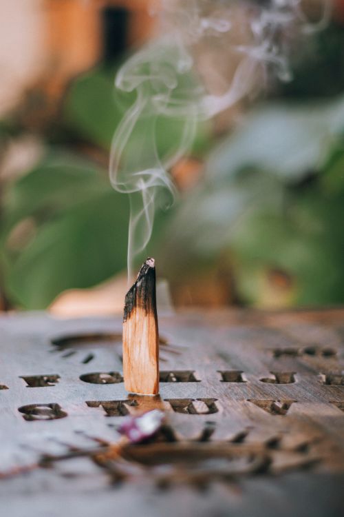 Free A burning wooden incense stick releasing aromatic smoke against a blurred natural backdrop. Stock Photo