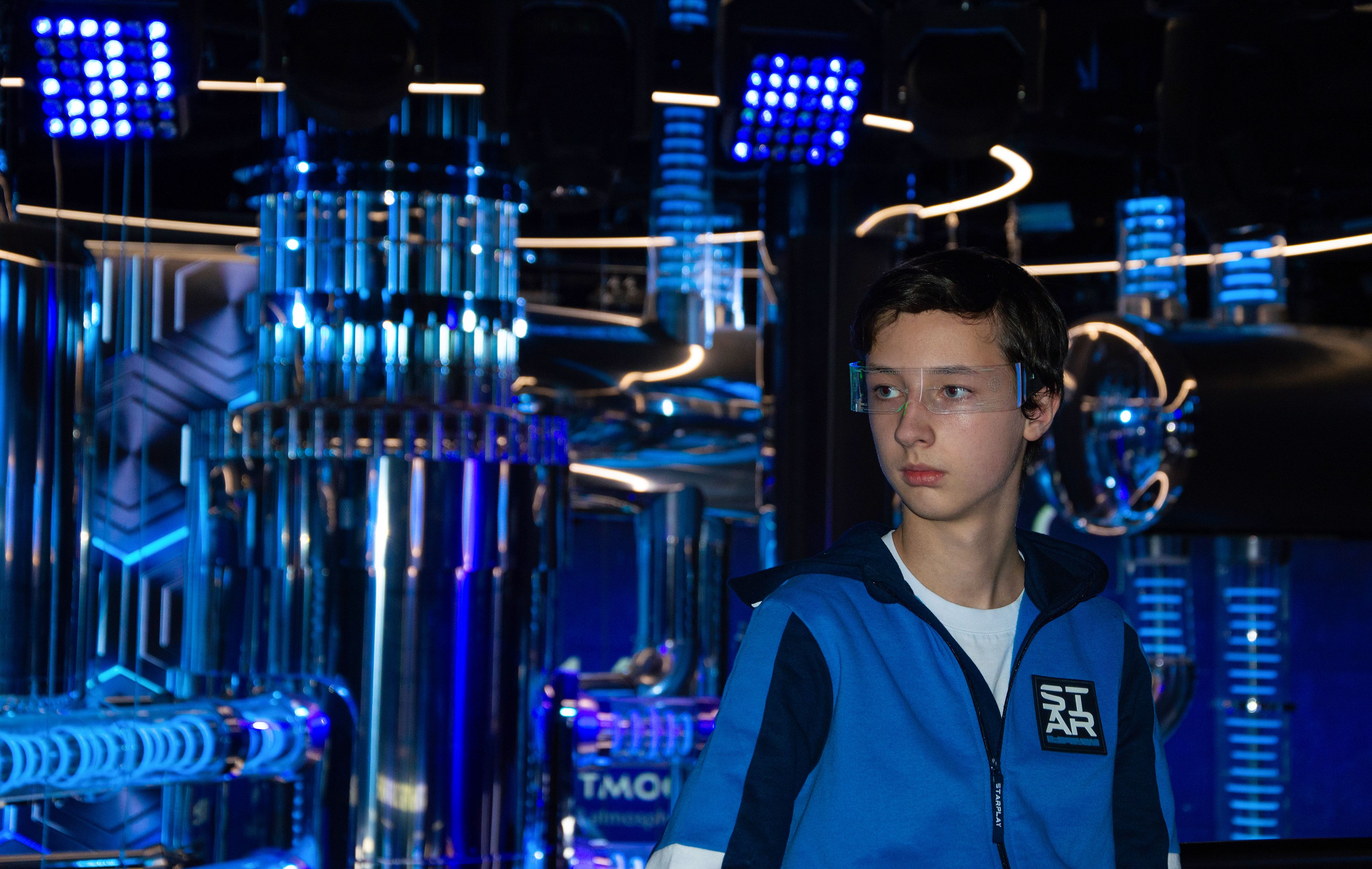 Teenager wearing protective eyewear in a high-tech laboratory environment with blue lighting.