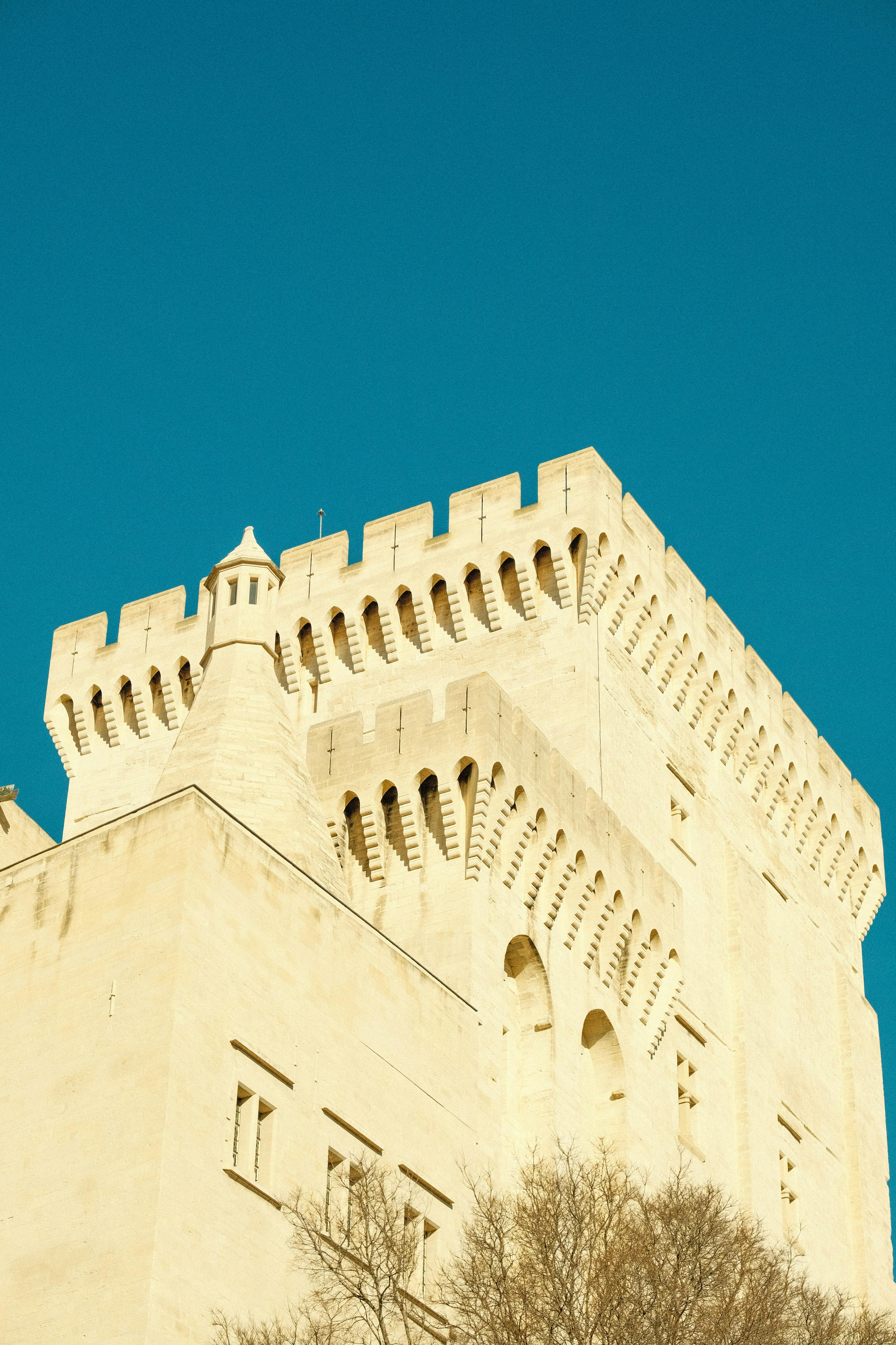 Sunlit medieval castle tower in urban setting with clear blue sky, captured from a low angle.