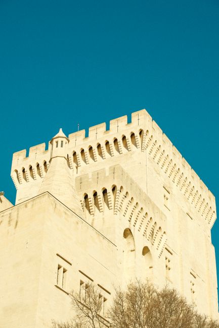 Sunlit medieval castle tower in urban setting with clear blue sky, captured from a low angle.