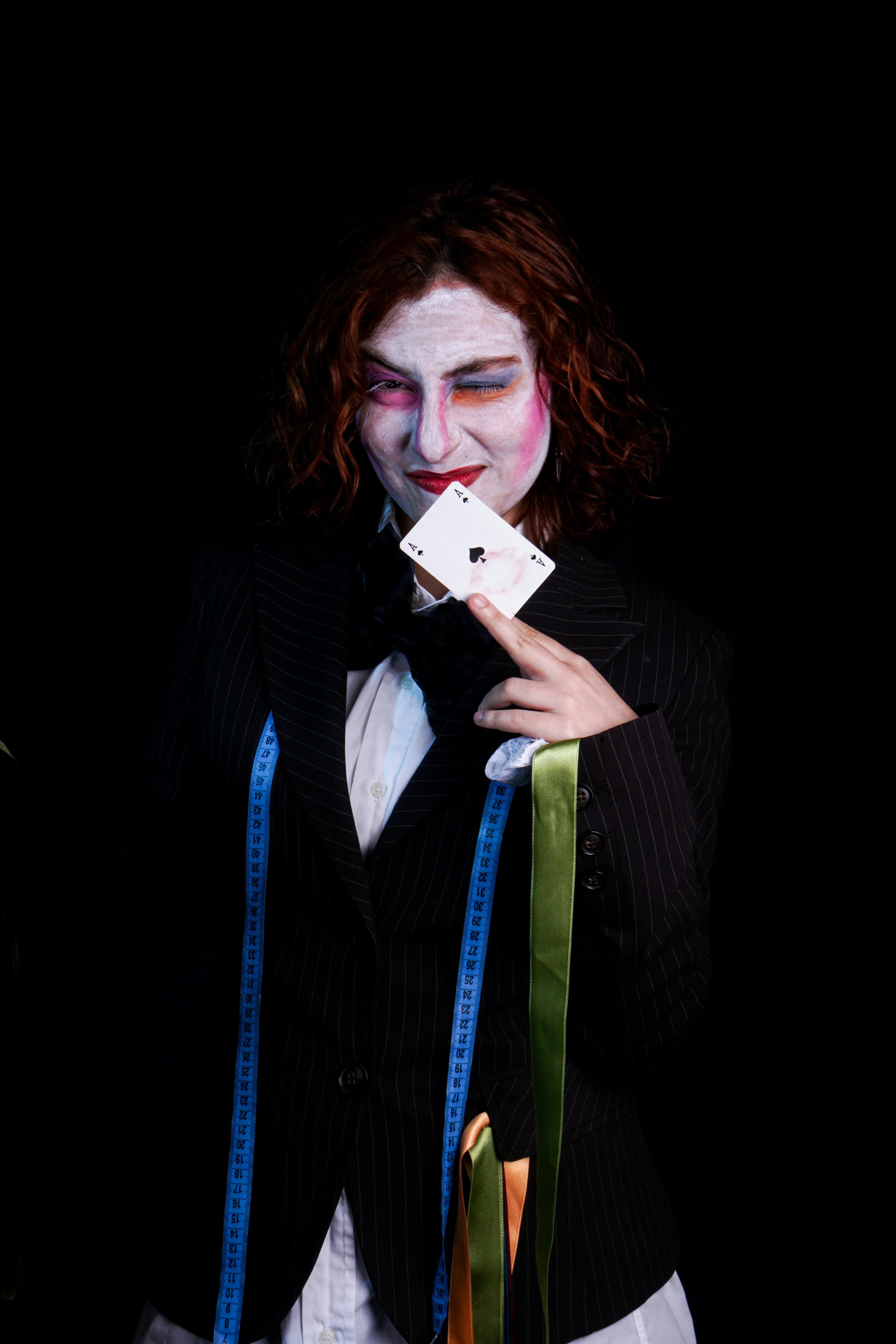 Free Woman in Joker-inspired costume holding playing cards against black background. Stock Photo