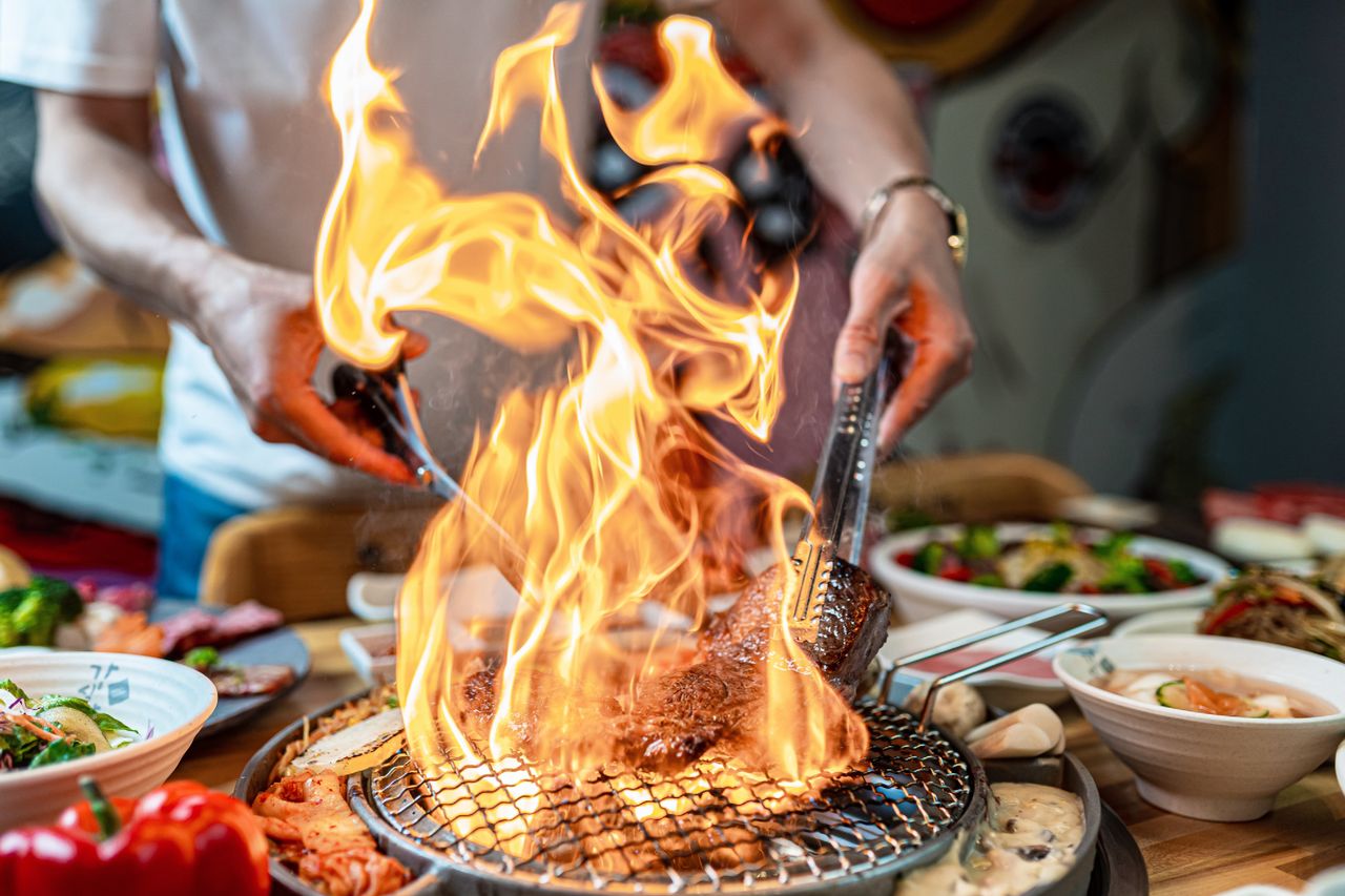 A chef cooking meat over fire on a table in front of guests