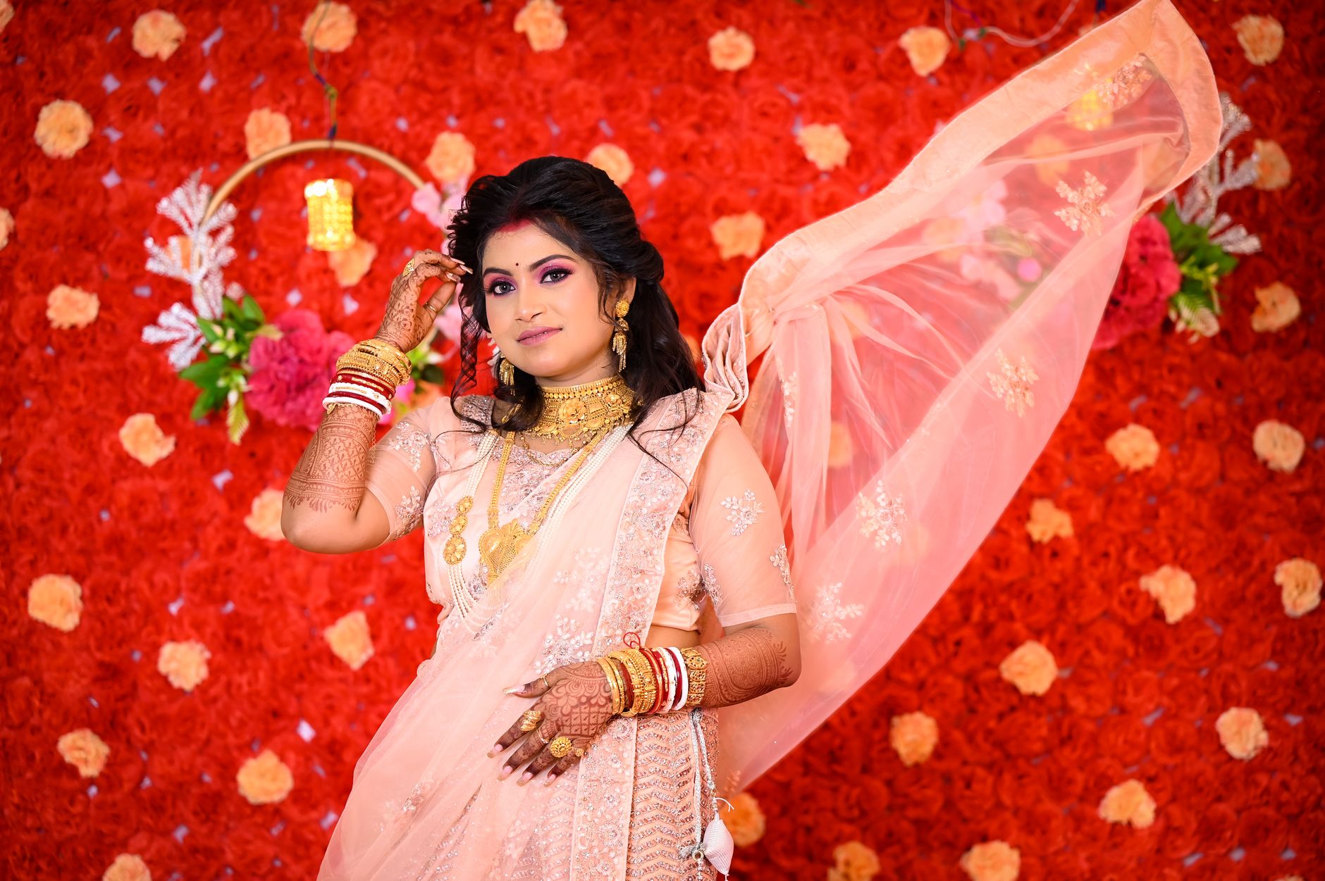 Stunning Indian bride in pink saree with henna tattoos against vibrant floral backdrop.