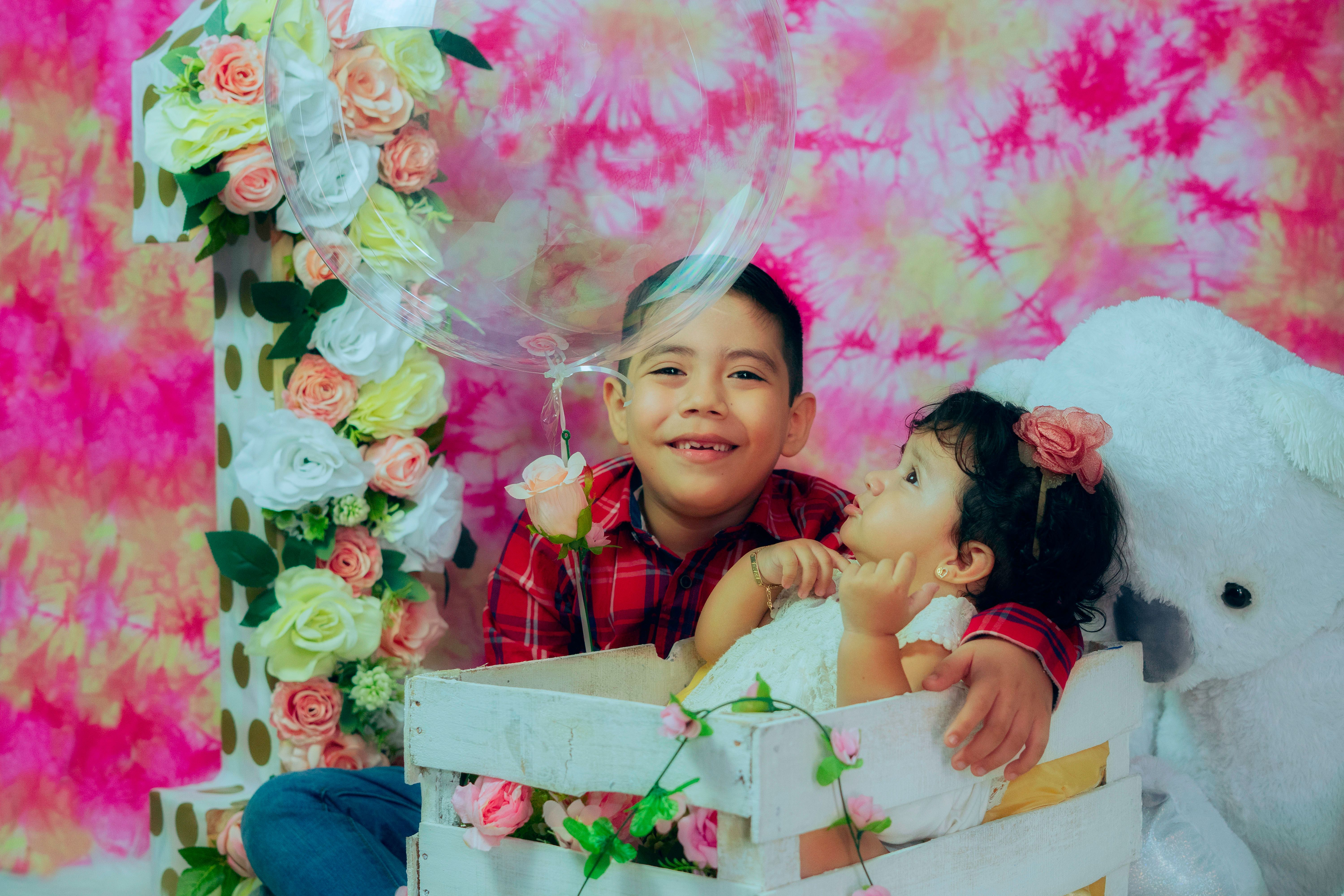 Fotomural Hermanos felices disfrutando de un momento juguetón con un globo y decoración floral.