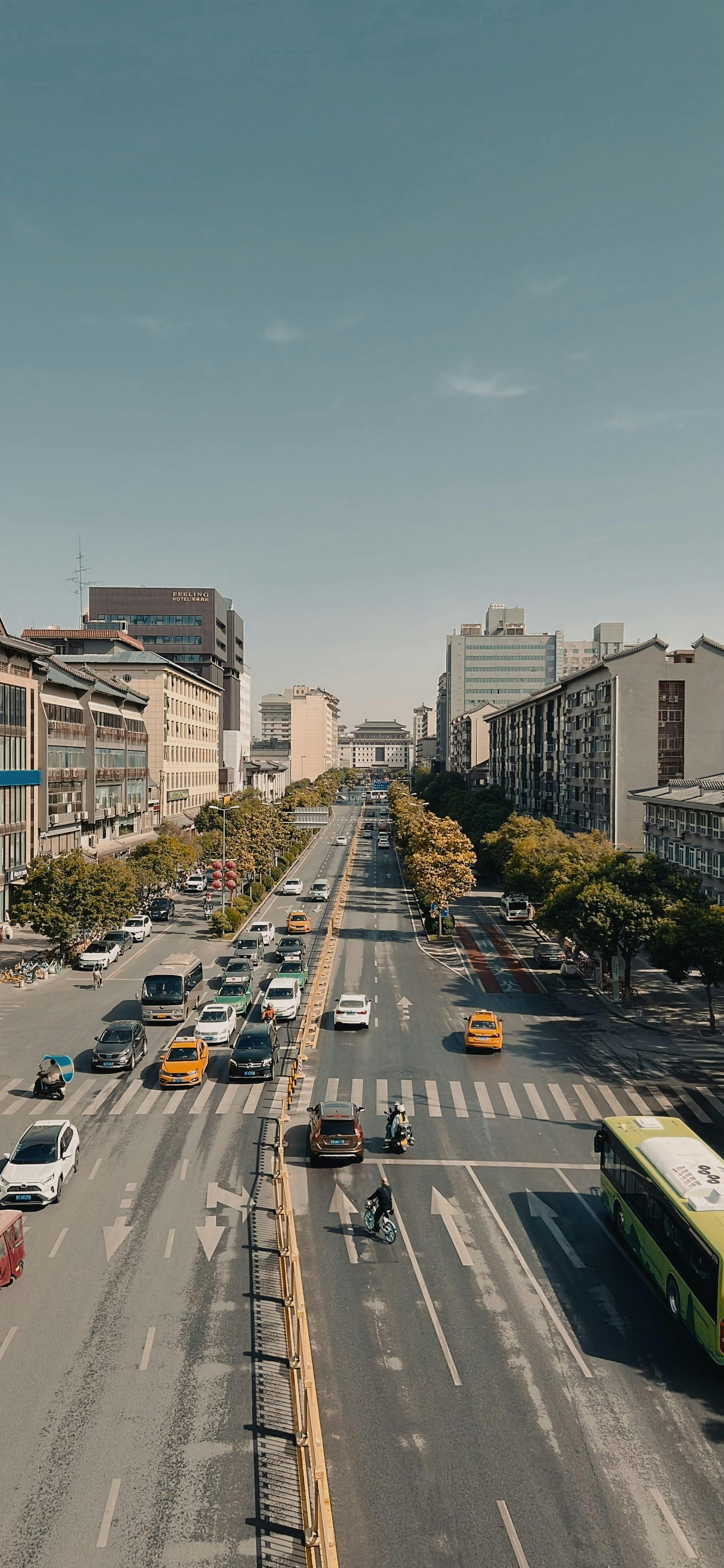 Aerial perspective of a bustling city street lined with vehicles under a clear sky.