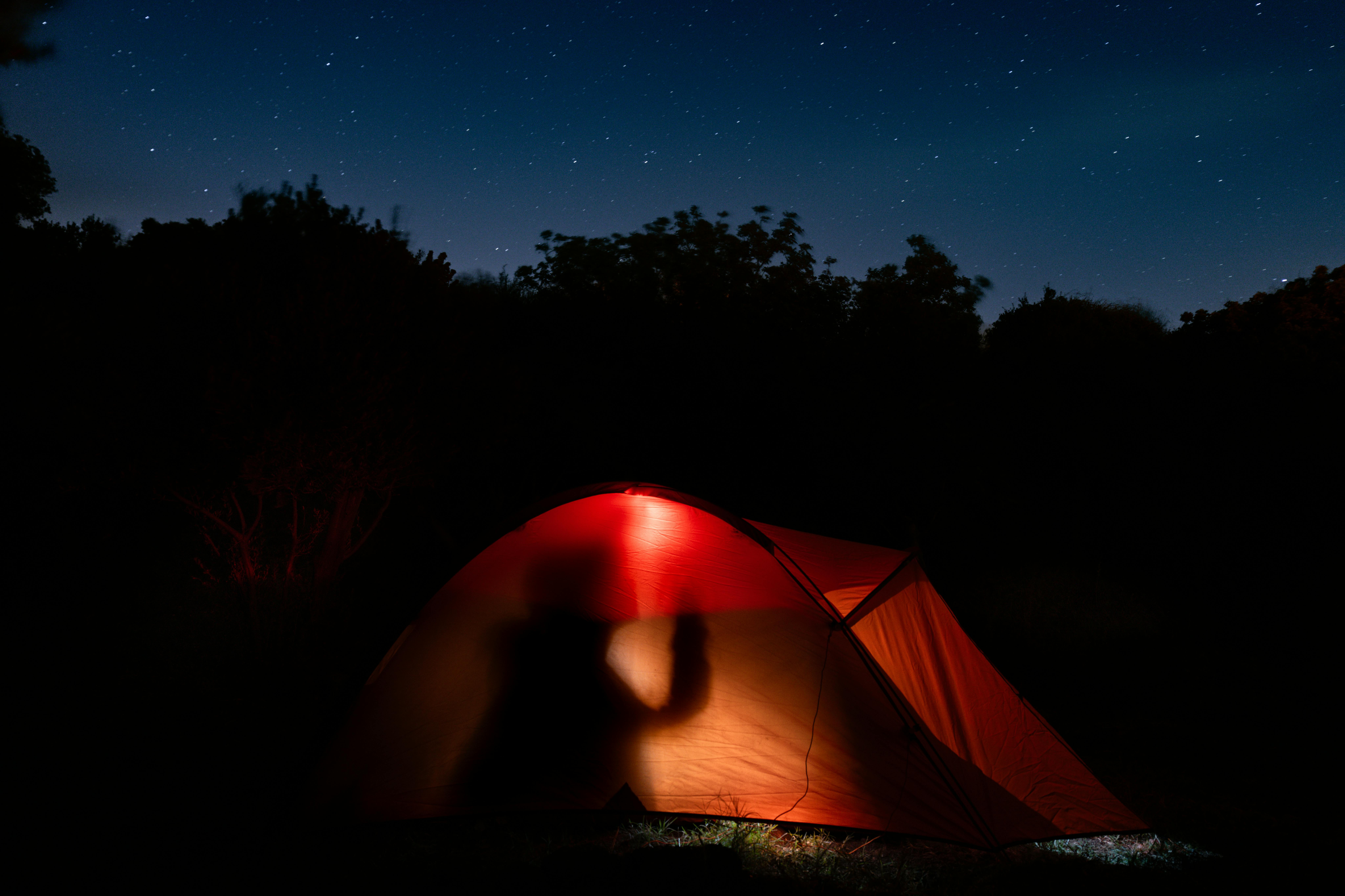 Silhouette camping under starry sky in Mudanya. A cozy illuminated tent amidst nature.