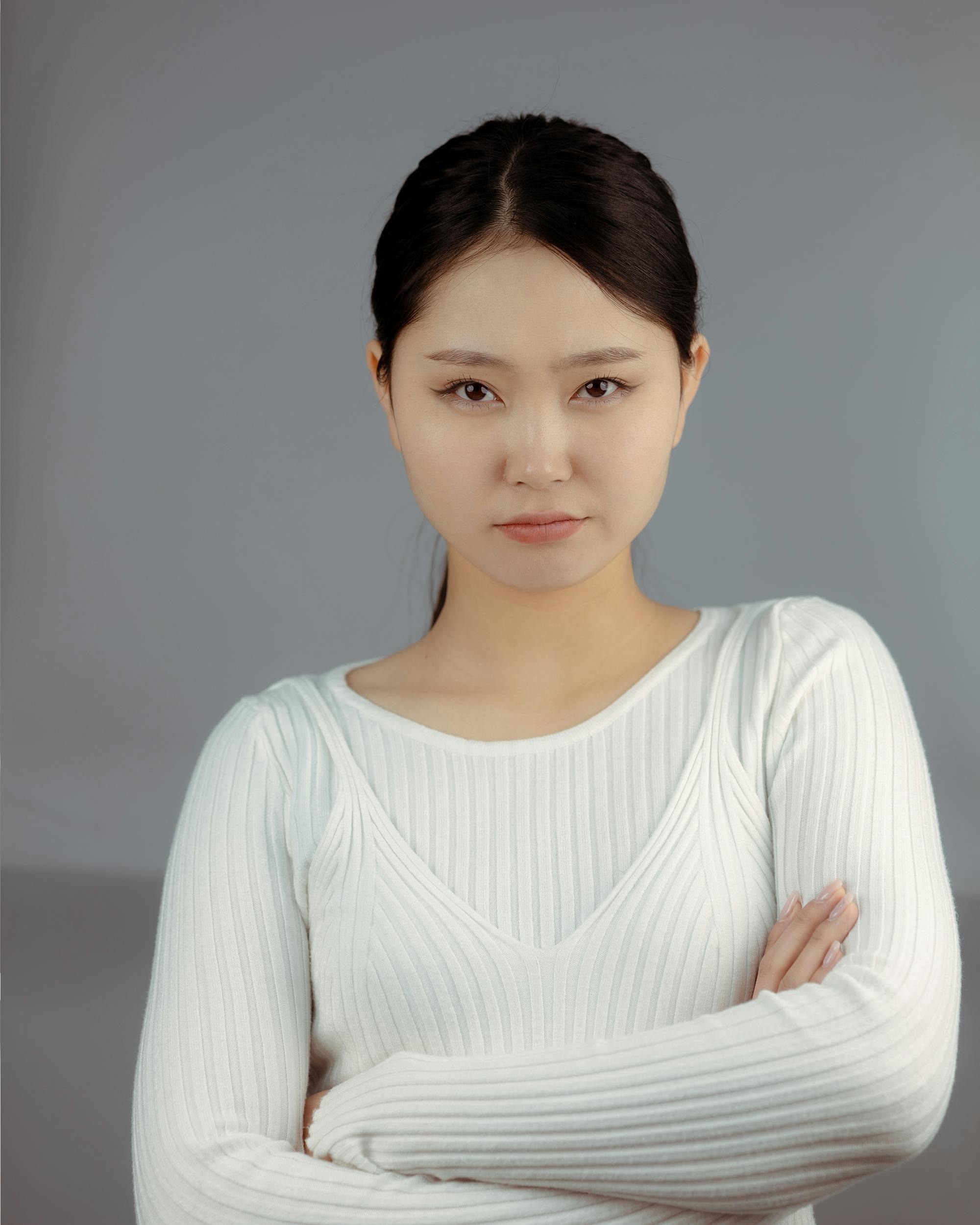 A confident woman stands with arms crossed in a fashion portrait with a gray backdrop.