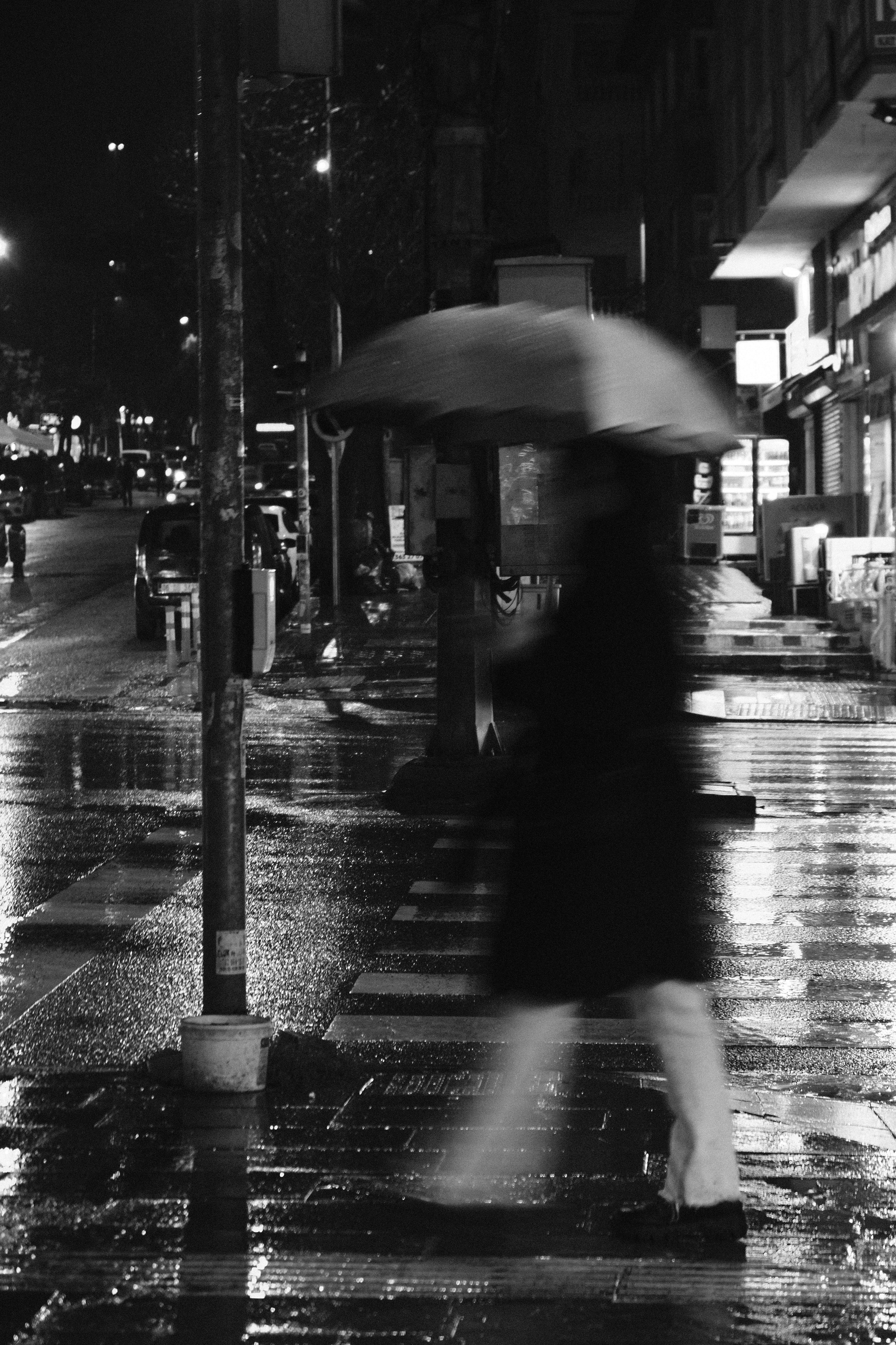 A person with an umbrella walks through a rainy city street at night, captured in blurred motion.