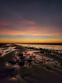 Tranquil beach at sunset with rocks and reflecting tide, capturing the beauty of nature.