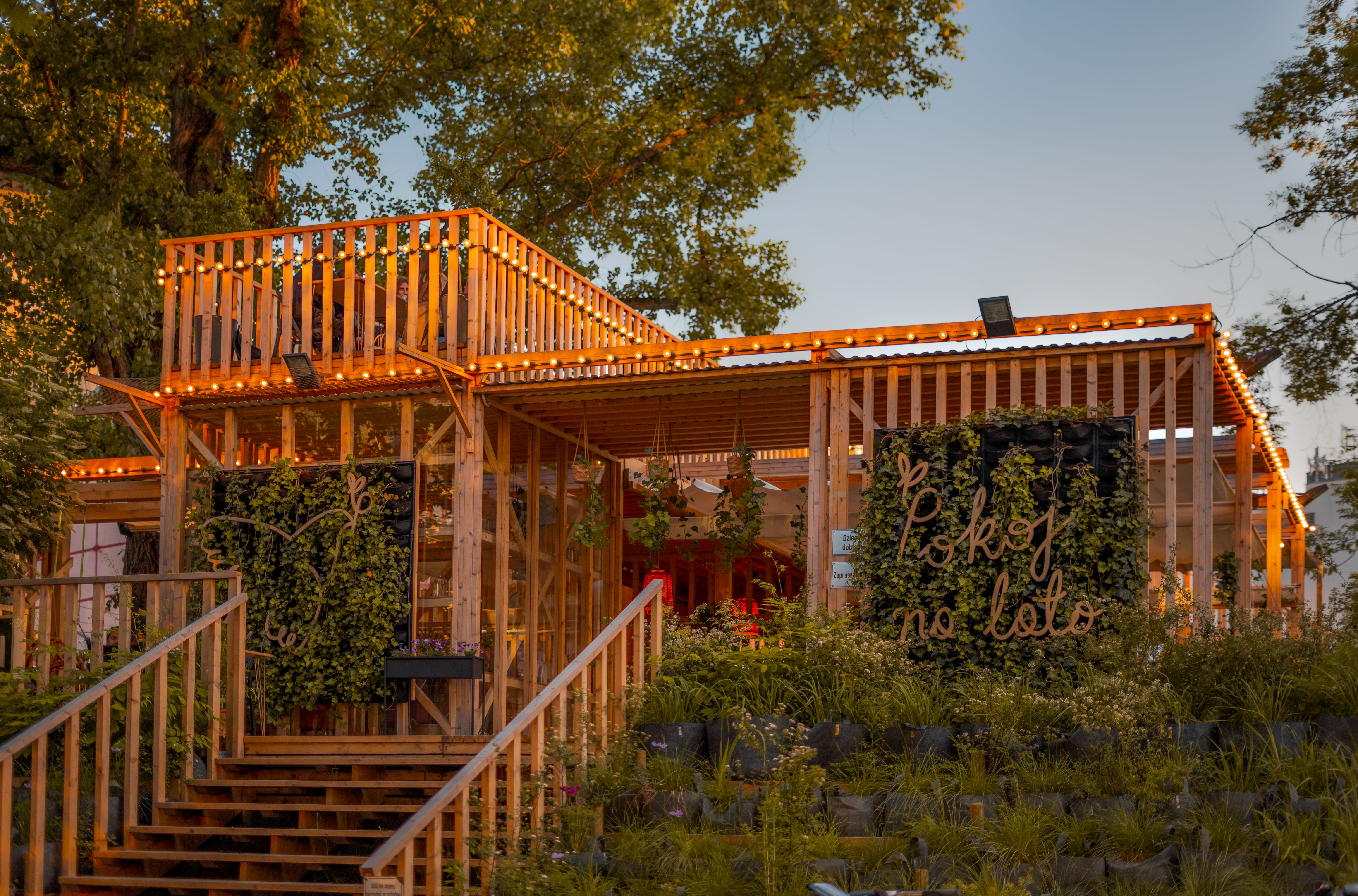 Outdoor wooden pavilion with lush garden and string lights at sunset, creating a warm and inviting atmosphere.