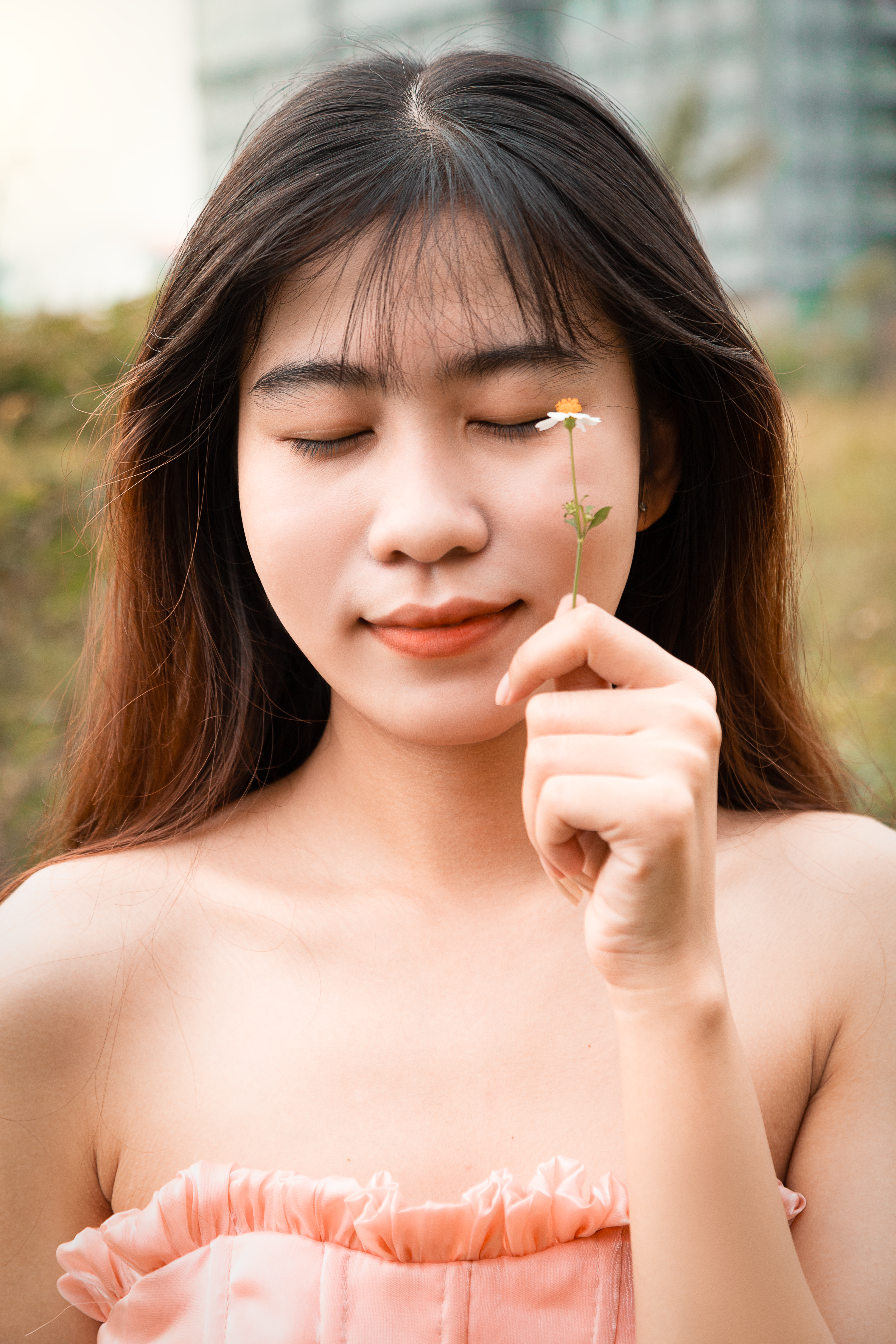Young woman holding a daisy with eyes closed, enjoying a peaceful moment outdoors.