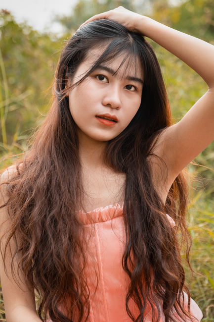 A graceful portrait of a young woman with long hair in nature, exuding warmth and charm.