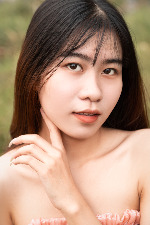 Free Close-up portrait of a young Asian woman with long black hair and a neutral expression, captured outdoors. Stock Photo