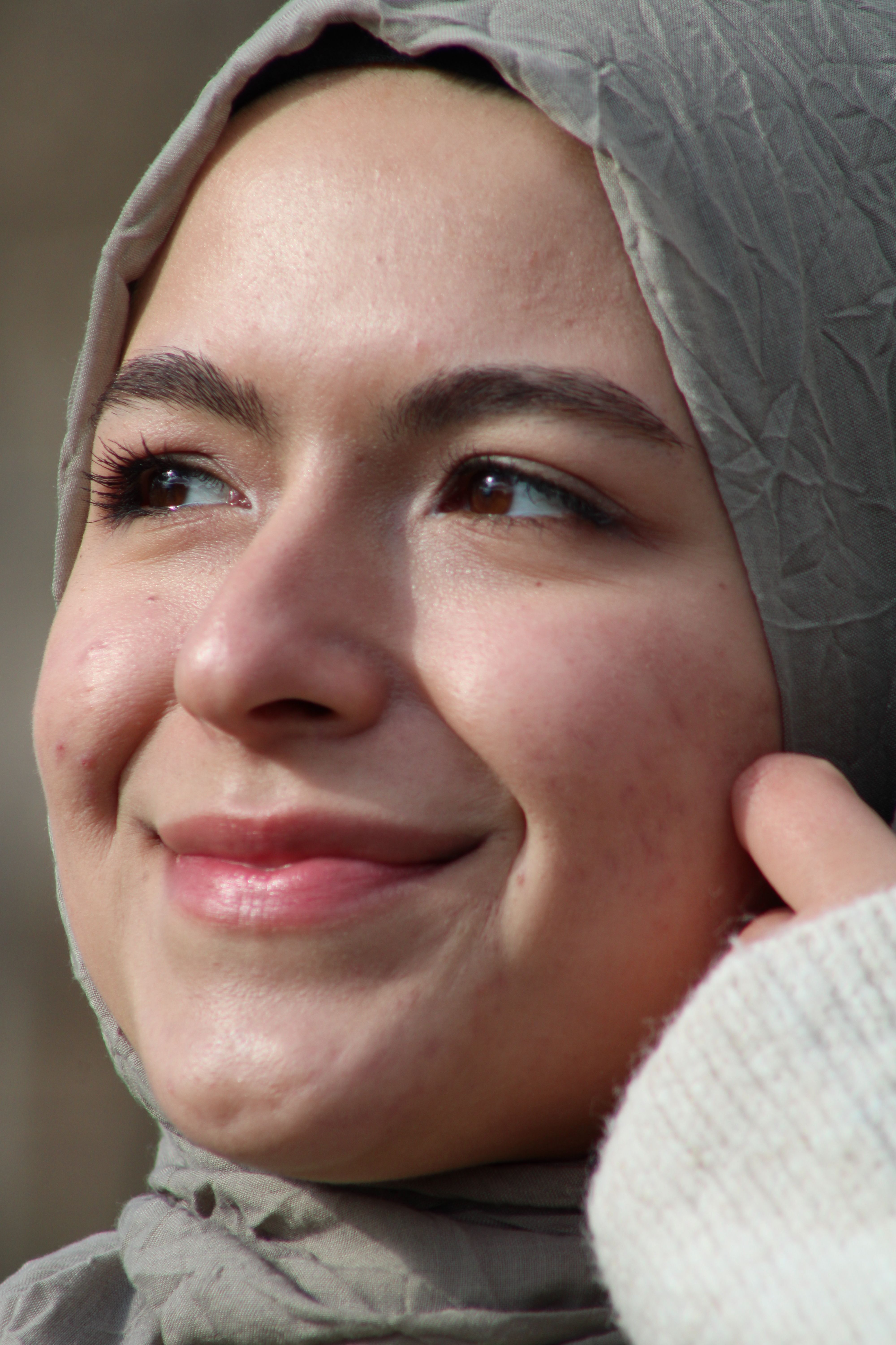 Close-up portrait of a smiling woman wearing a hijab outdoors, radiating joy.