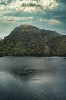 Tranquil mountain lake surrounded by lush greenery under dramatic skies.