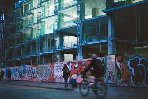 A man riding a bike past a building with graffiti on it