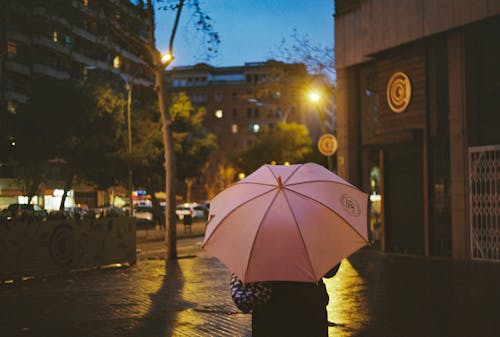 A person holding a pink umbrella walking down a street