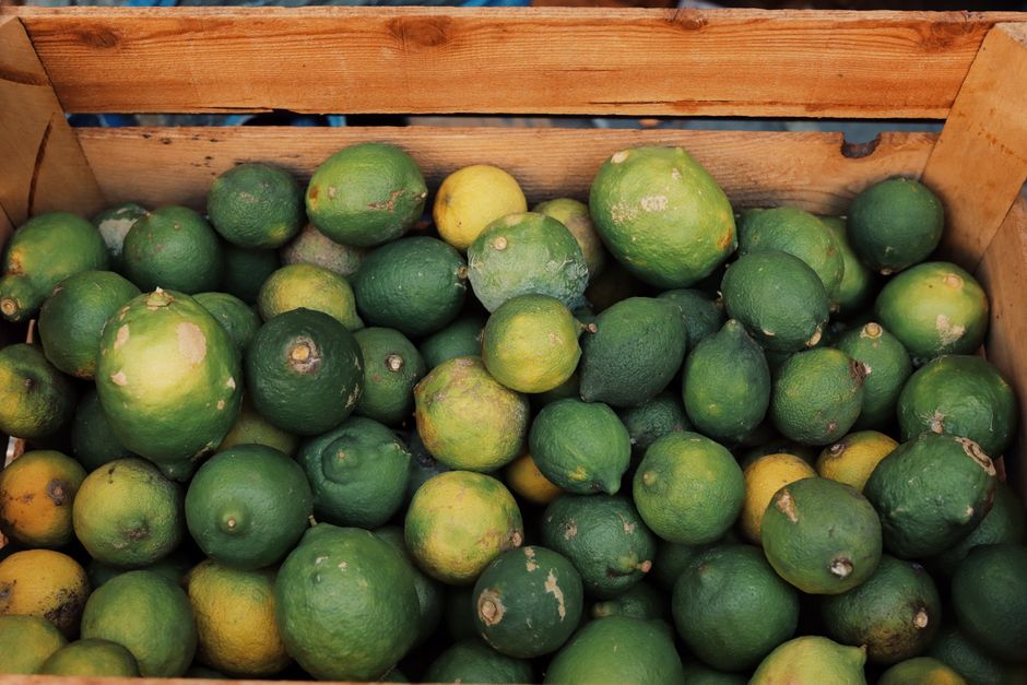 A collection of fresh green lemons in a rustic wooden box at a market in Palermo, Sicily.