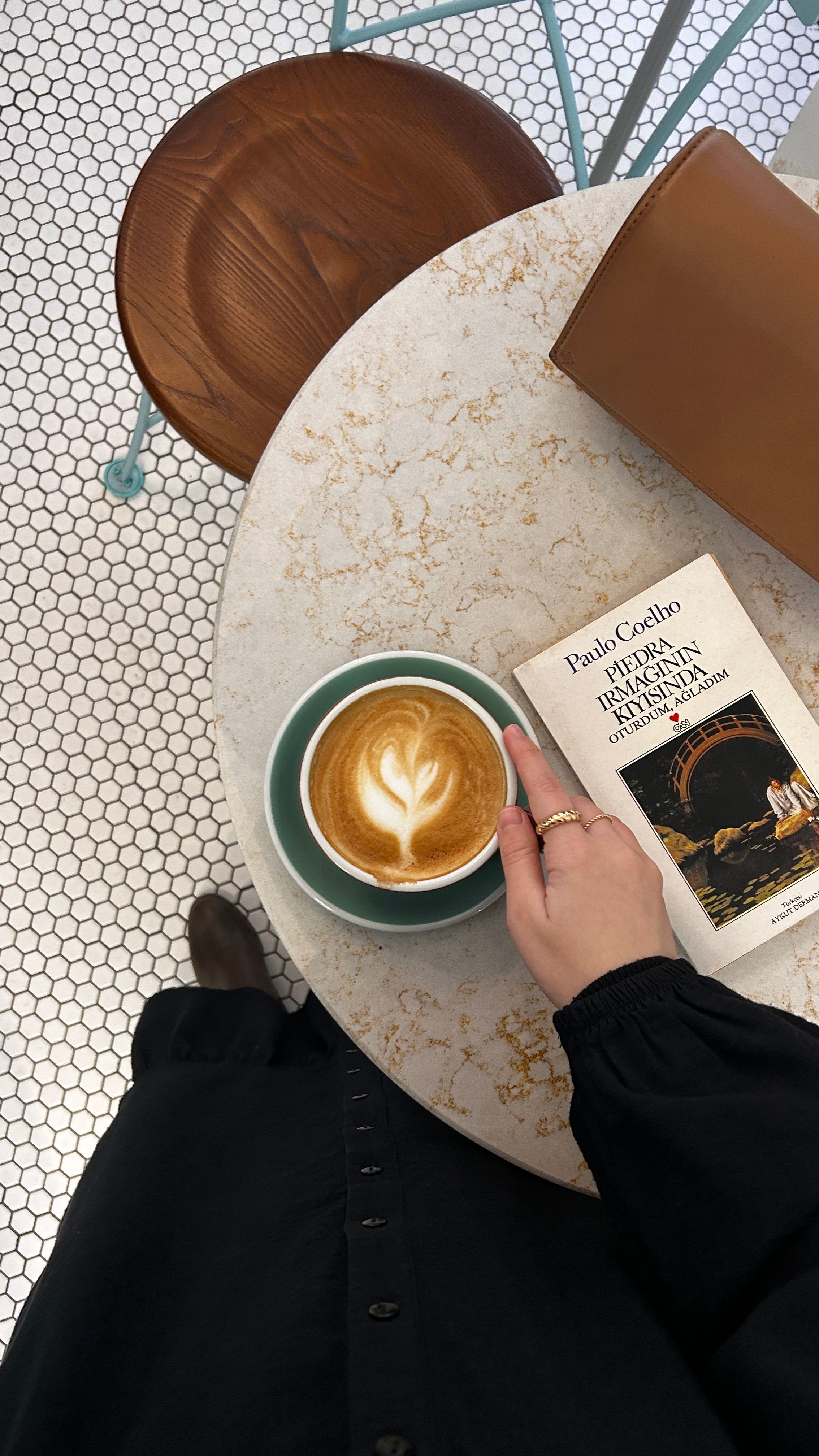 Top view of a latte and book on a cafe table, held by a woman. Ideal for lifestyle or coffee content.
